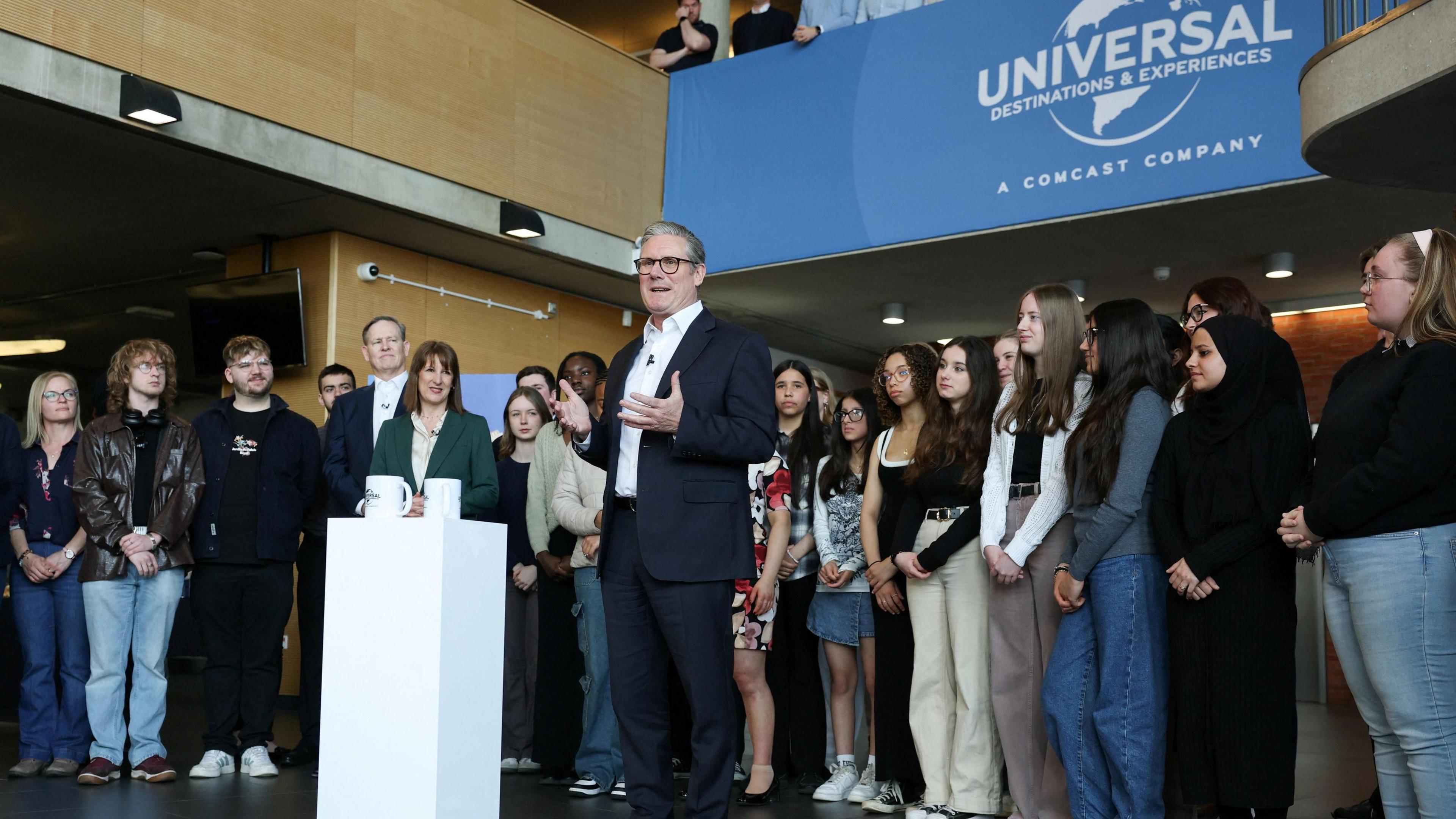 Prime Minister Sir Keir Starmer speaking to a gathered crowd of young student during a visit to Bedford. A blue Universal banner is on the balcony behind him.