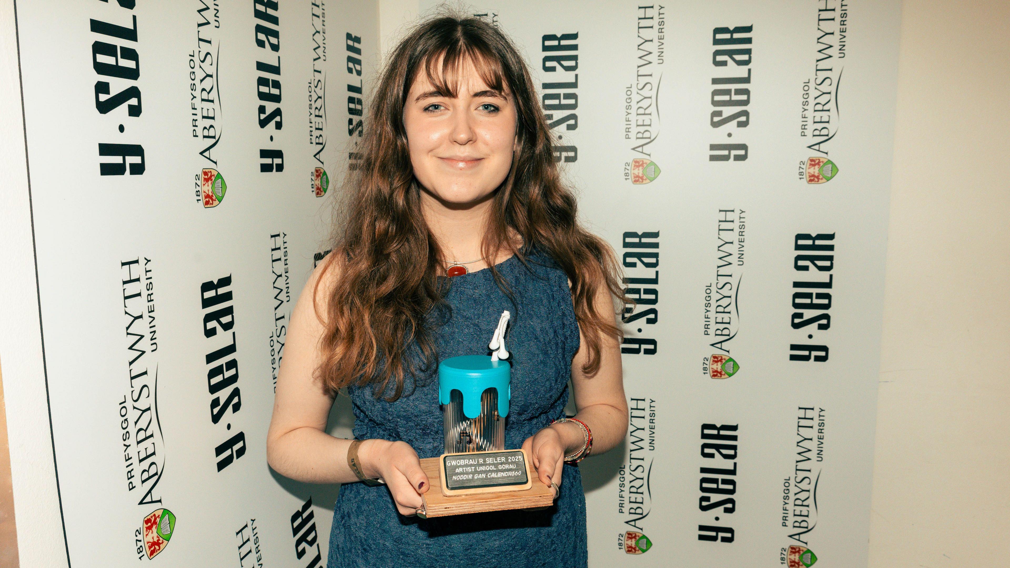 Llun o Buddug yn gafael yn un o'r gwobrau a enillodd yng Ngwobrau'r Selar