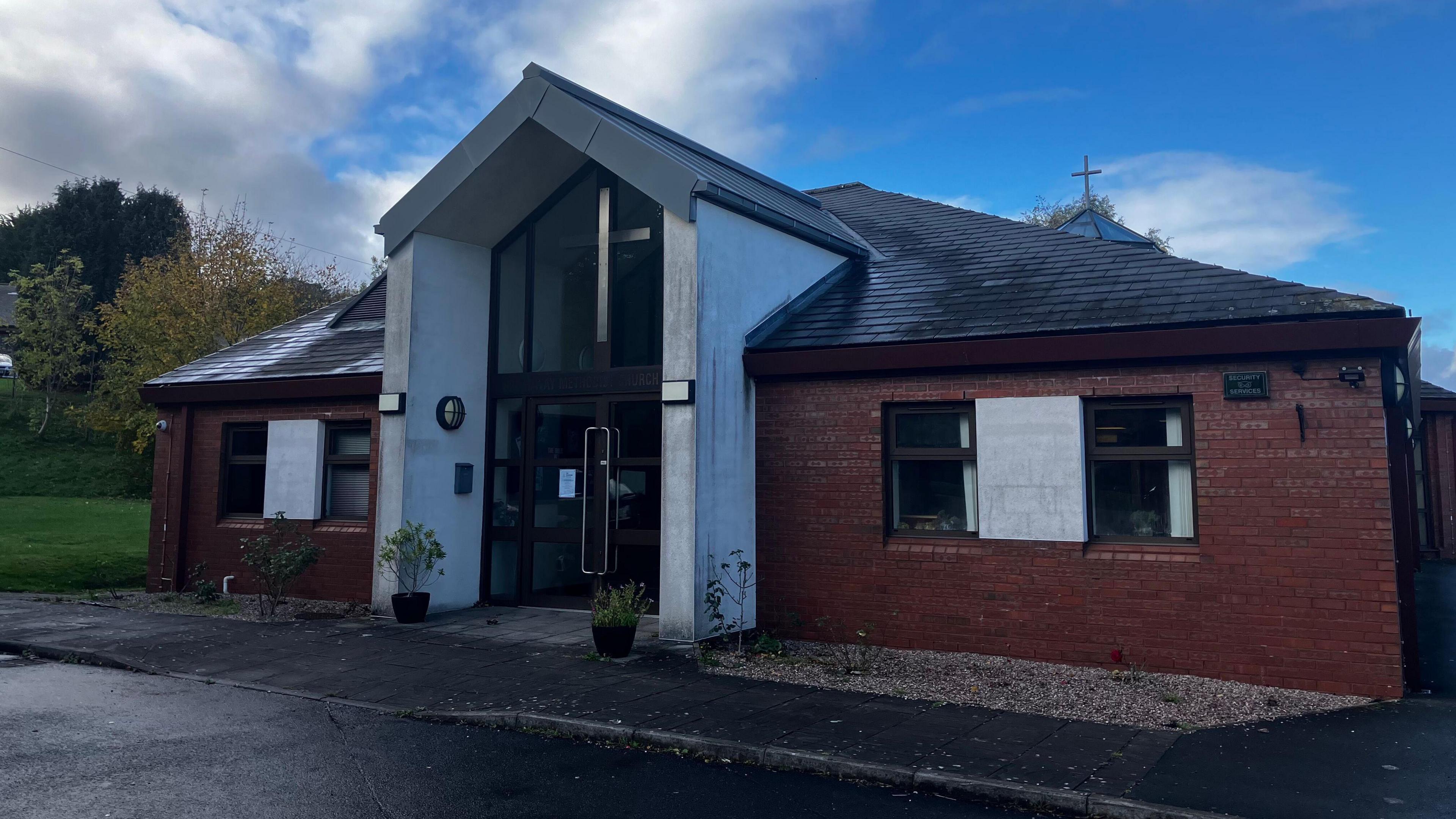 A brick building with a white opening in the front. the top of the door is adorned with a big silver cross.