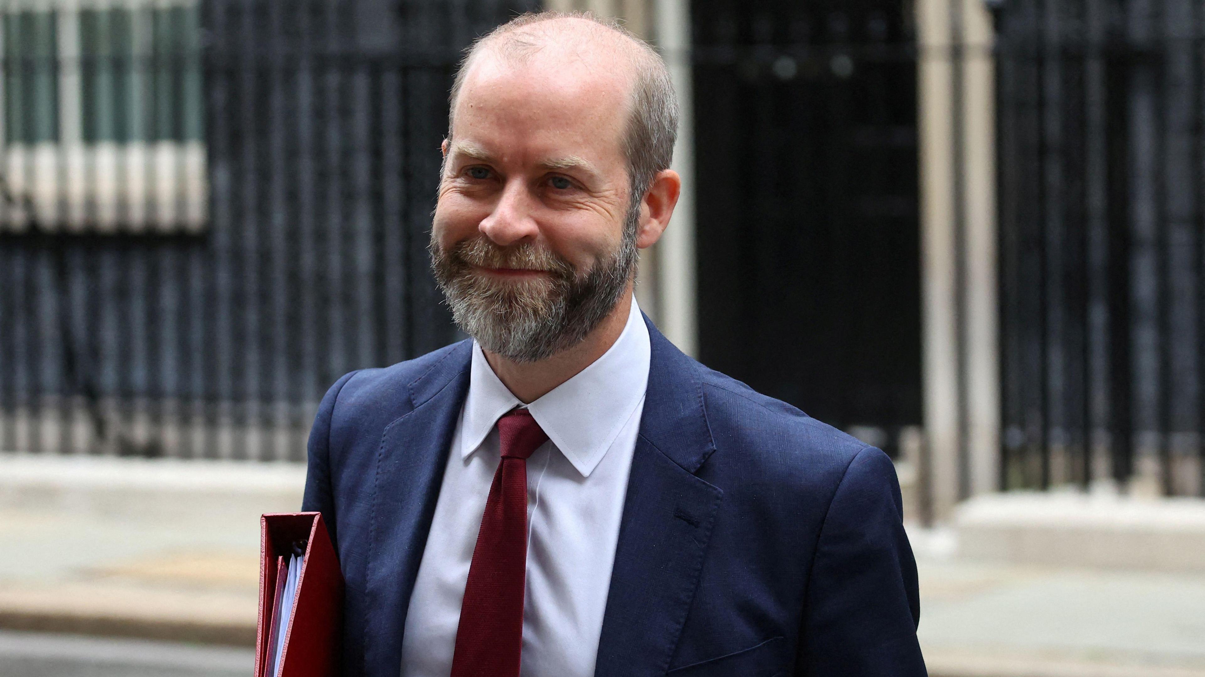 Jonathan Reynolds walking up Downing Street wearing a suit and tie and carrying a red folder.  