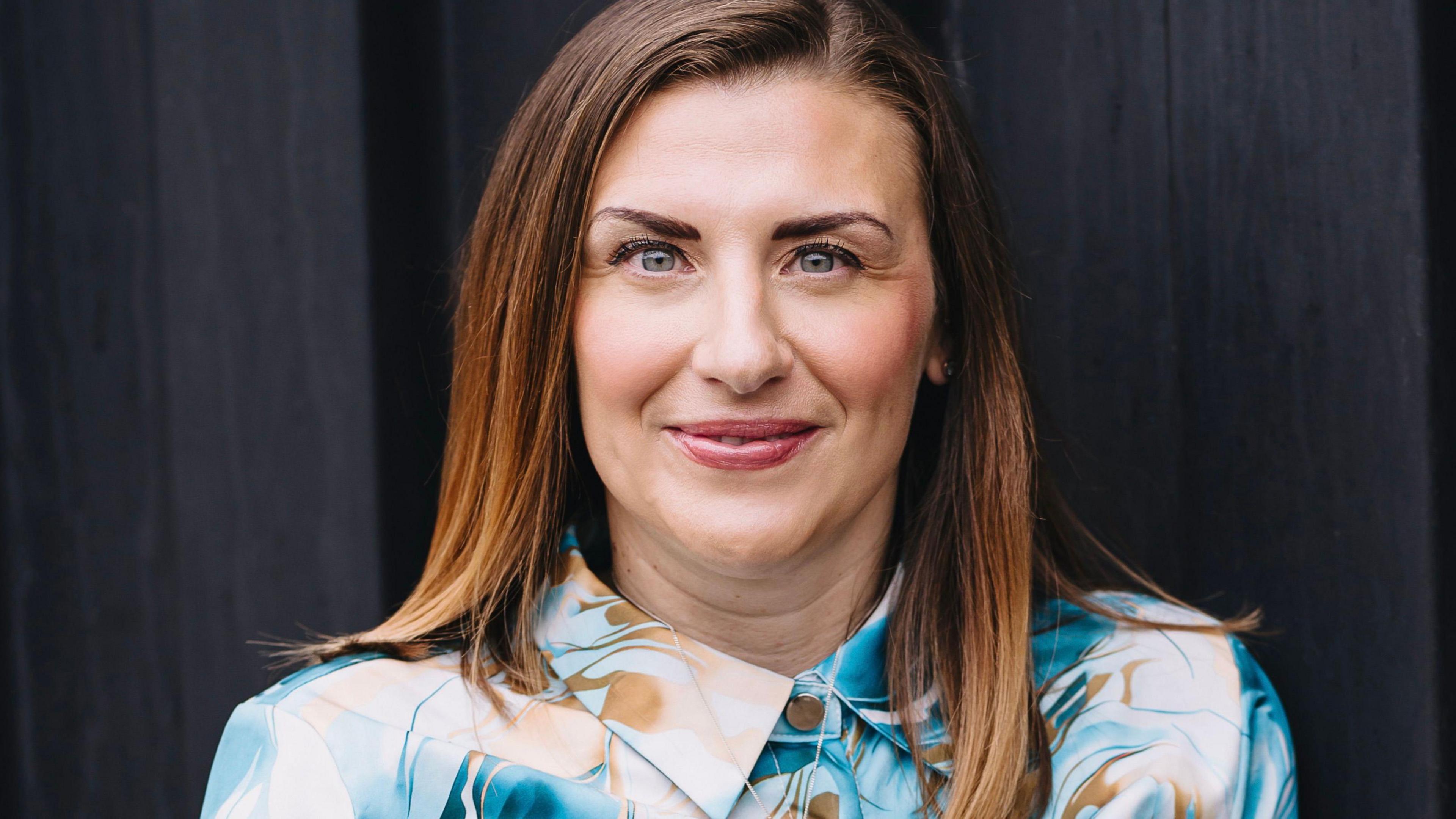 Kathryn Williams is wearing a blue and brown shirt and is staring straight at the camera.