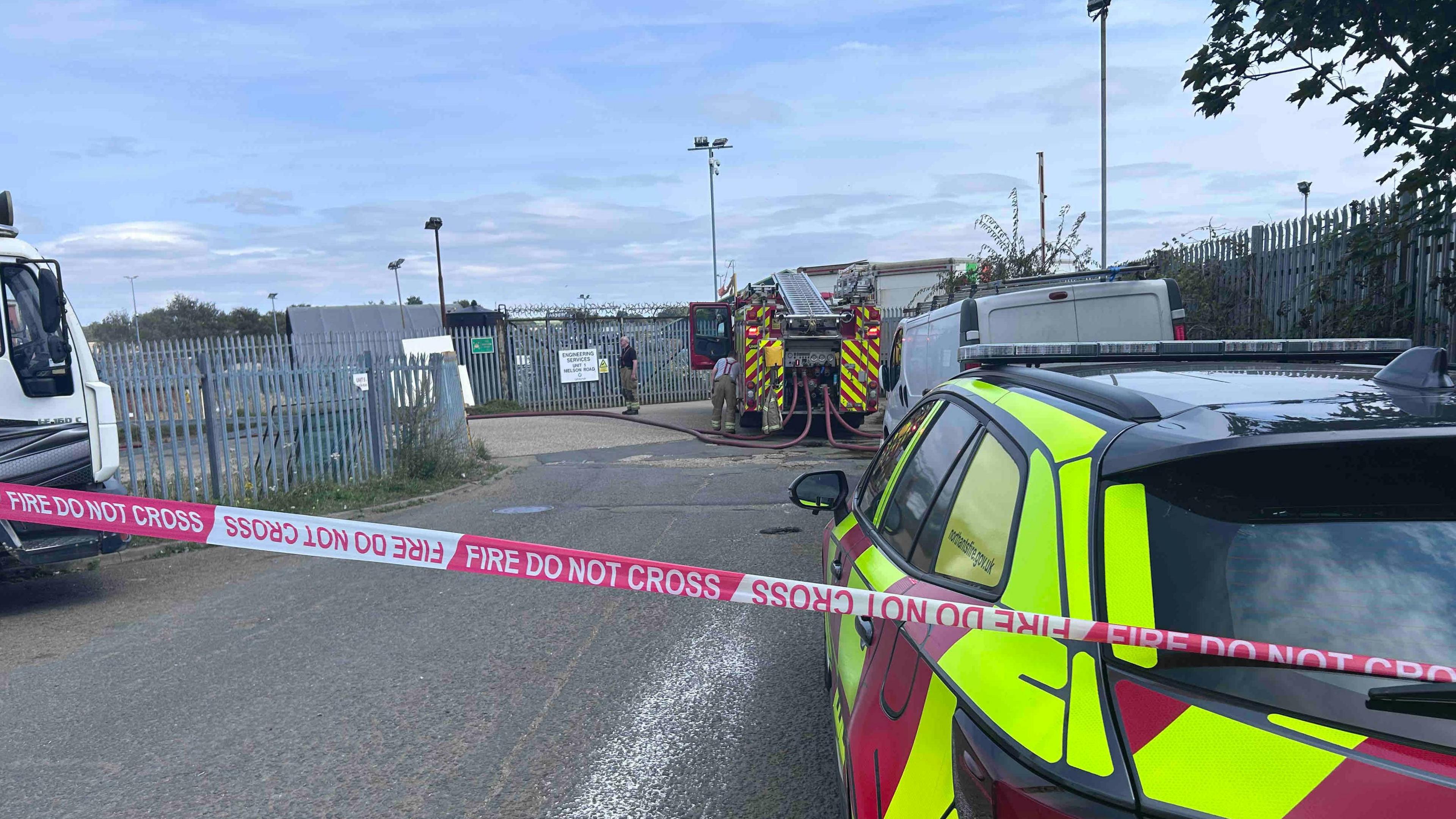 A red and white cordon is in pace which reads 'Fire do not cross'. Behind it is a fire engine and a red and white fire support vehicle.