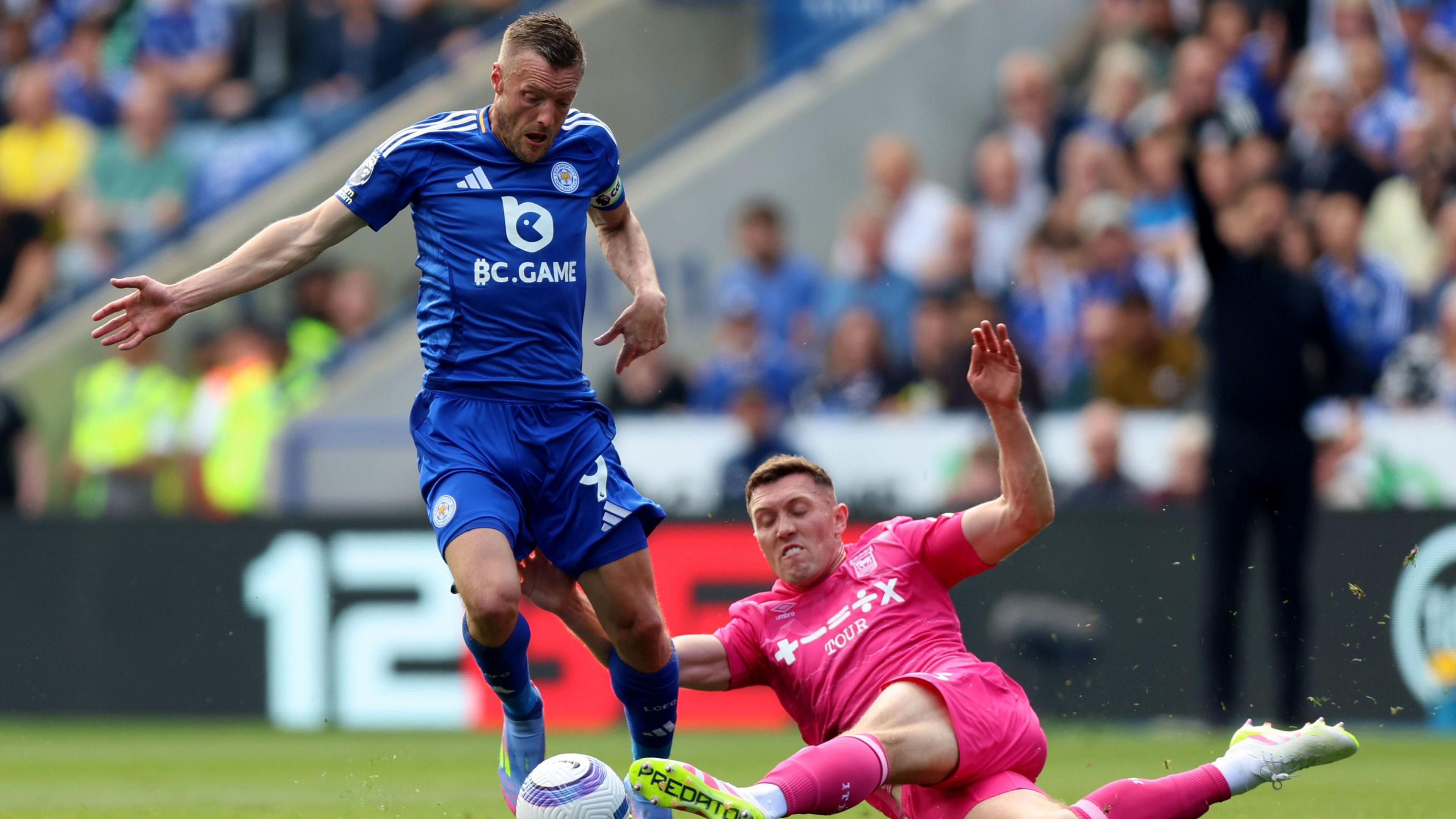 Ipswich Town's Dara O'Shea attempts to tackle Leicester's Jamie Vardy mid match. Vardy wears a blue strip with O'Shea in a pink Town away strip. 