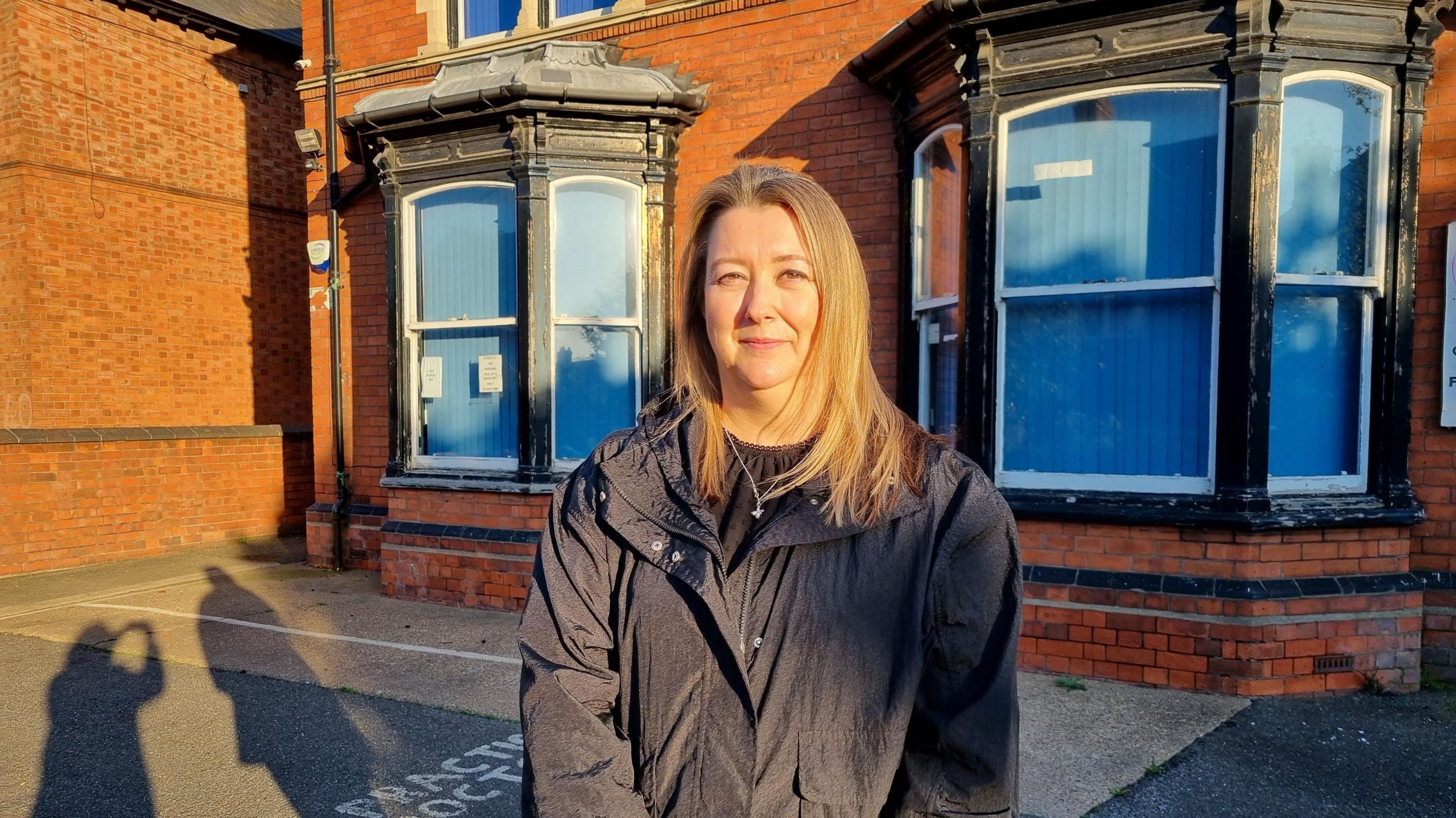 Emma Milligan stands in front of a red brick building that used to be a GP practice