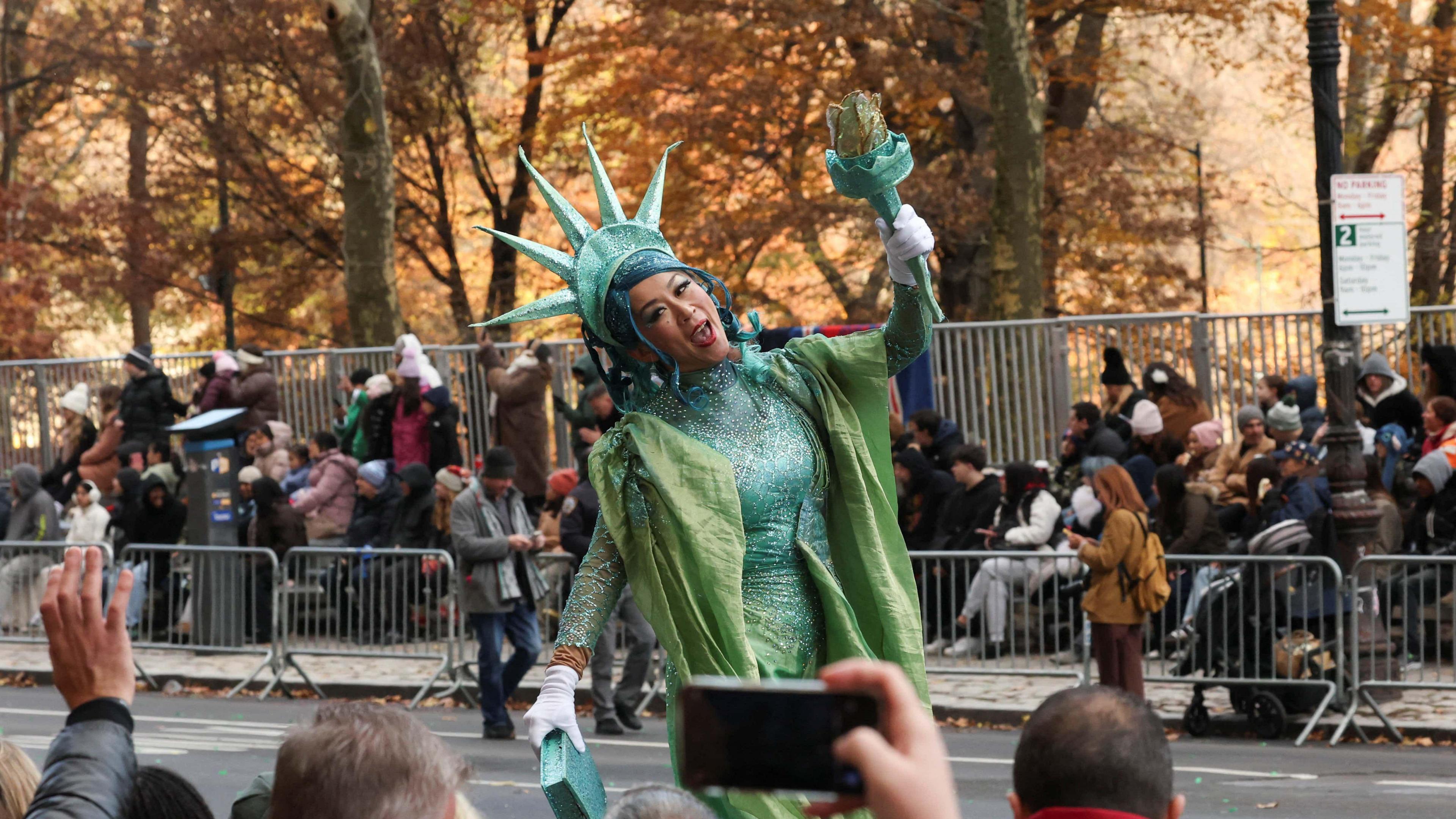 A woman dressed as the statue of liberty walks down the street, performing for the crowd.
