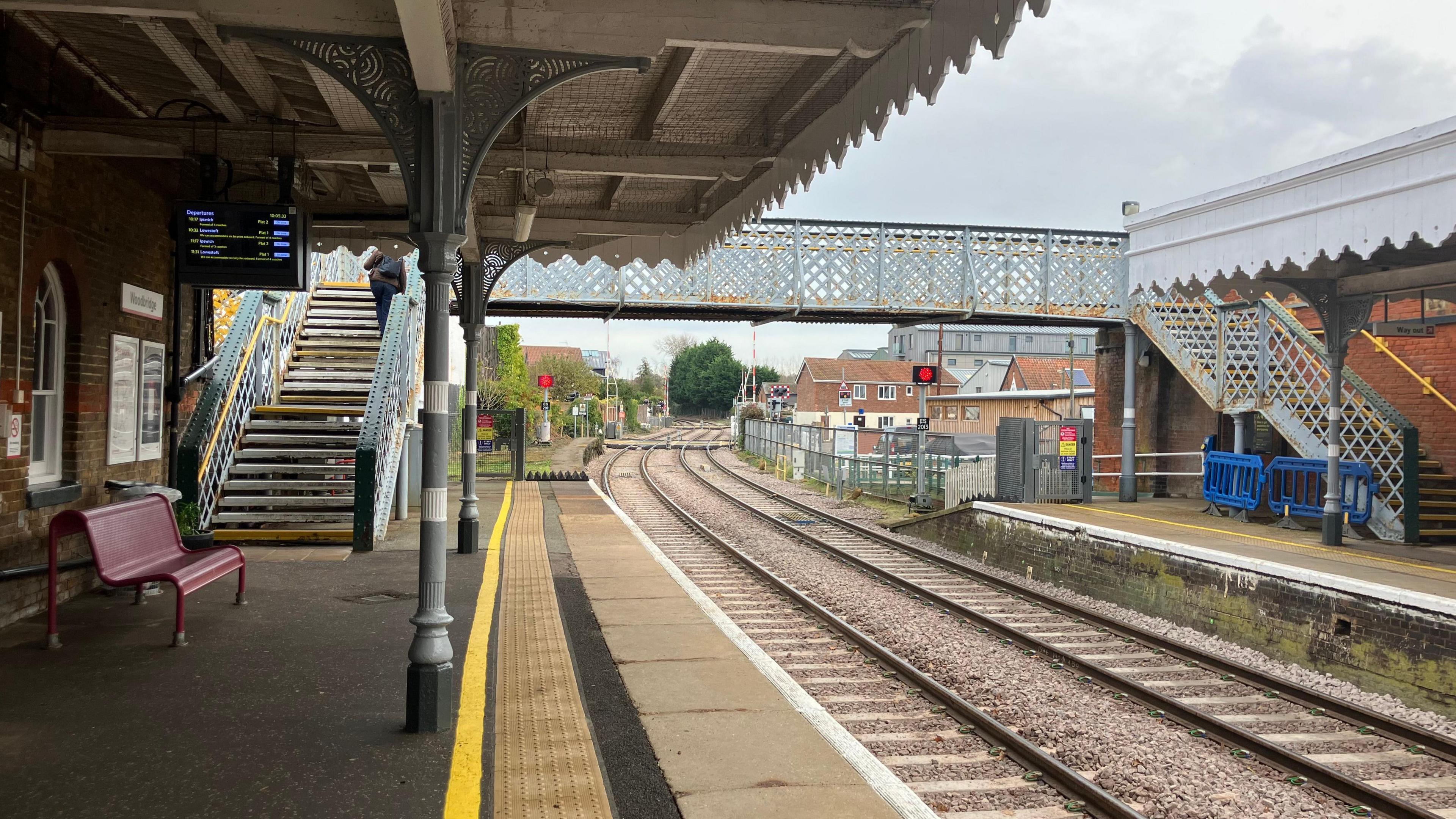 A view of the Woodbridge railway station from the left hand platform. The footbridge between the two platforms can be seen in the distance. Railway tracks split two platforms.