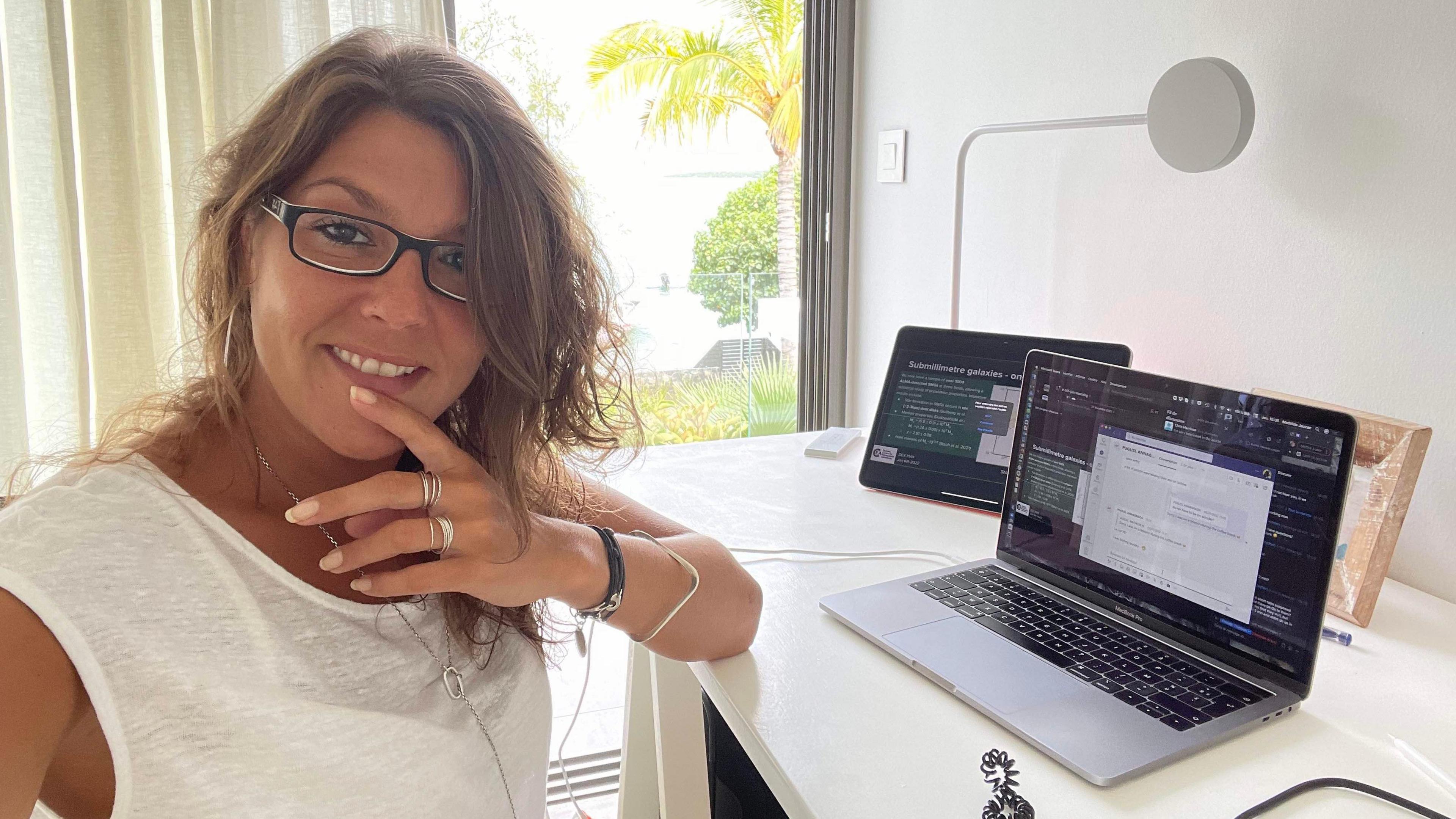 Prof Mathilde Jauzac sitting at her desk. A laptop and tablet are on her white desk. She is facing the camera and smiling. She has long brown hair and is wearing dark rimmed glasses.