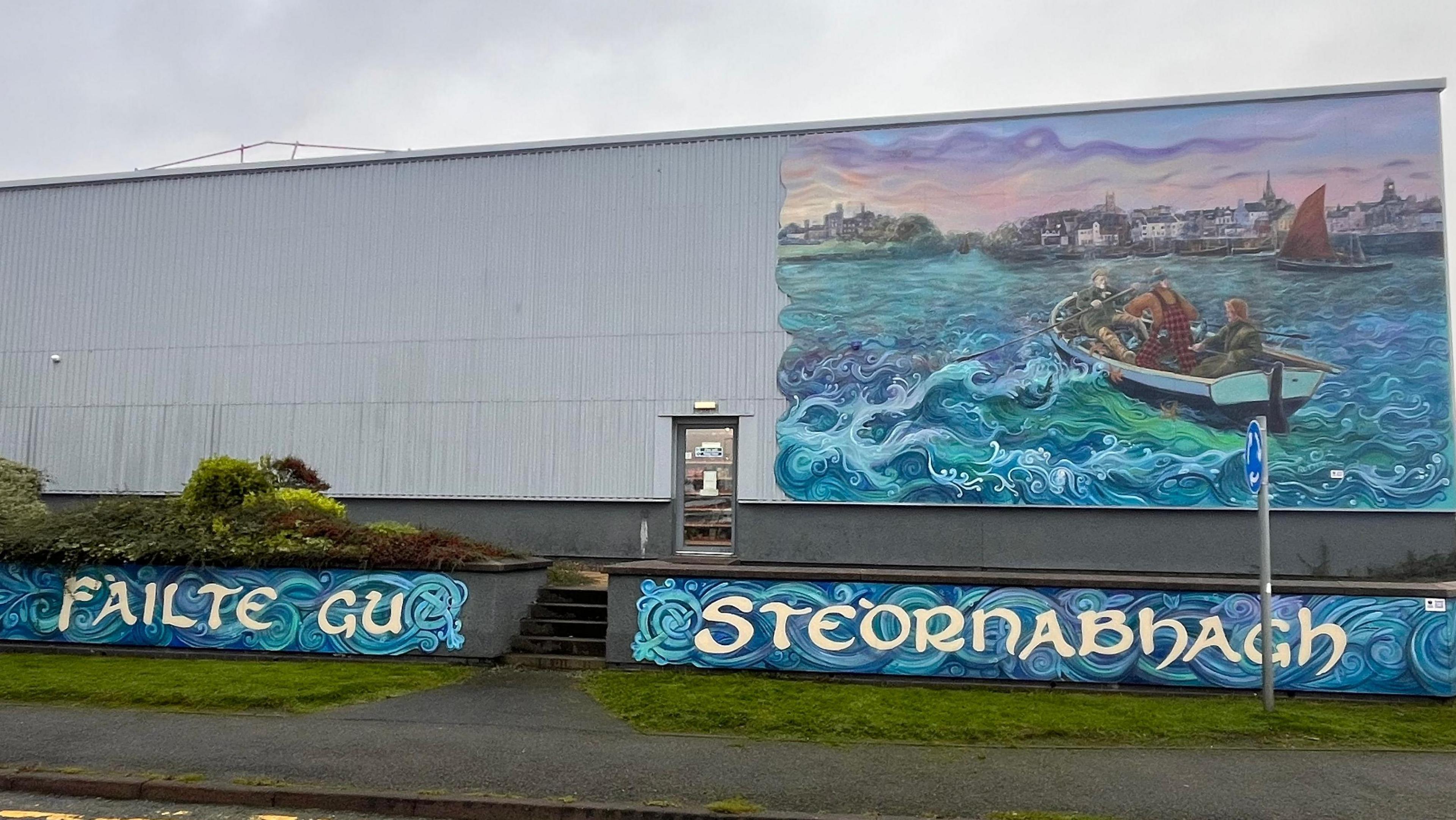 Ìomhaigh den dealbh-balla ùr a tha air nochdadh ann an Steòrnabhagh, le Fàilte gu Steòrnabhagh sgrìobhte air agus dealbh de bhàta aig muir agus cuid de thogalaichean Steòrnabhaigh san dealbh cuideachd.