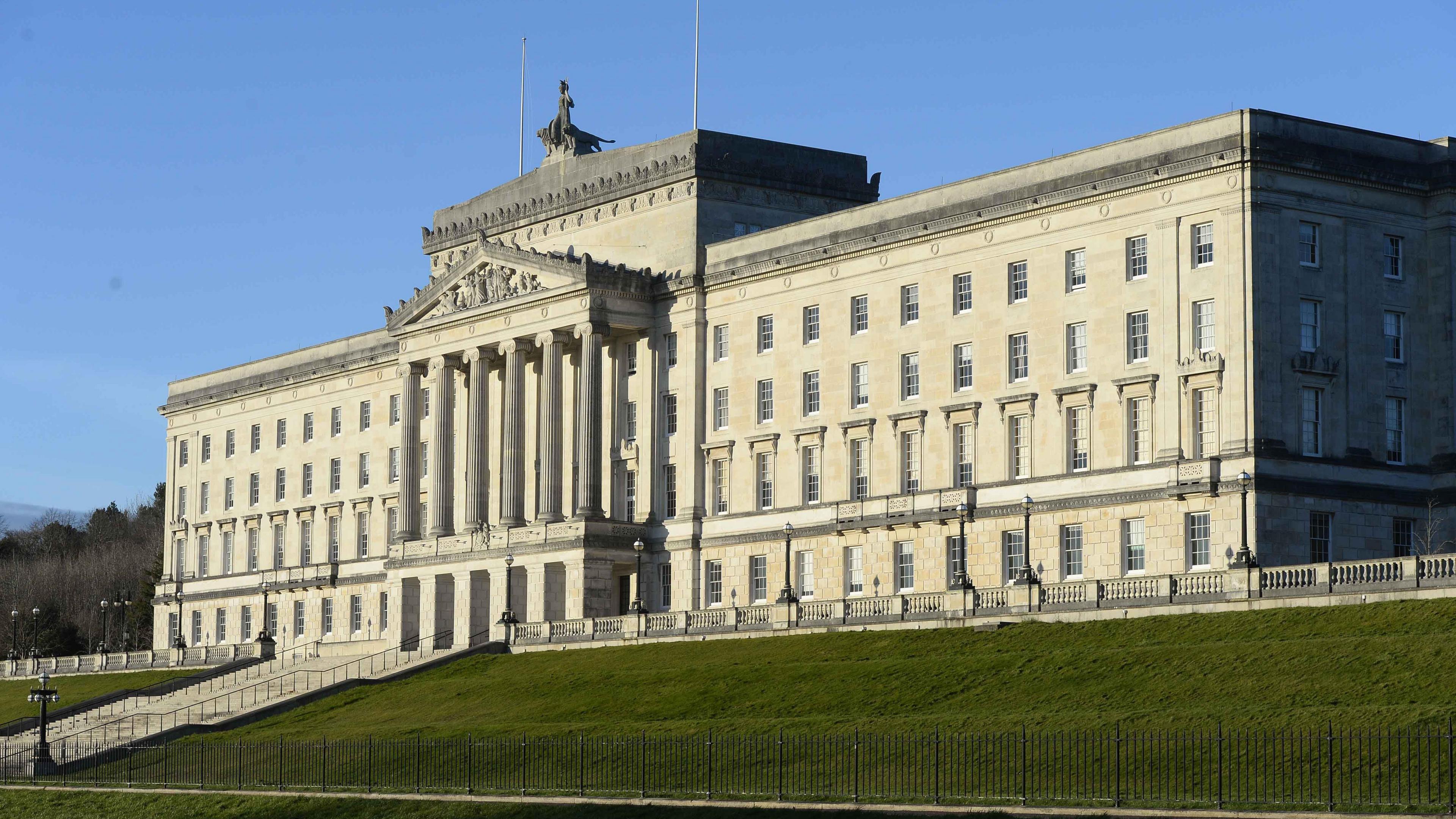 A large white building sits on top of a sloped green mound. White stone steps split the mound and lead up to the building. There are 6 large pillars don't the middle of the building.