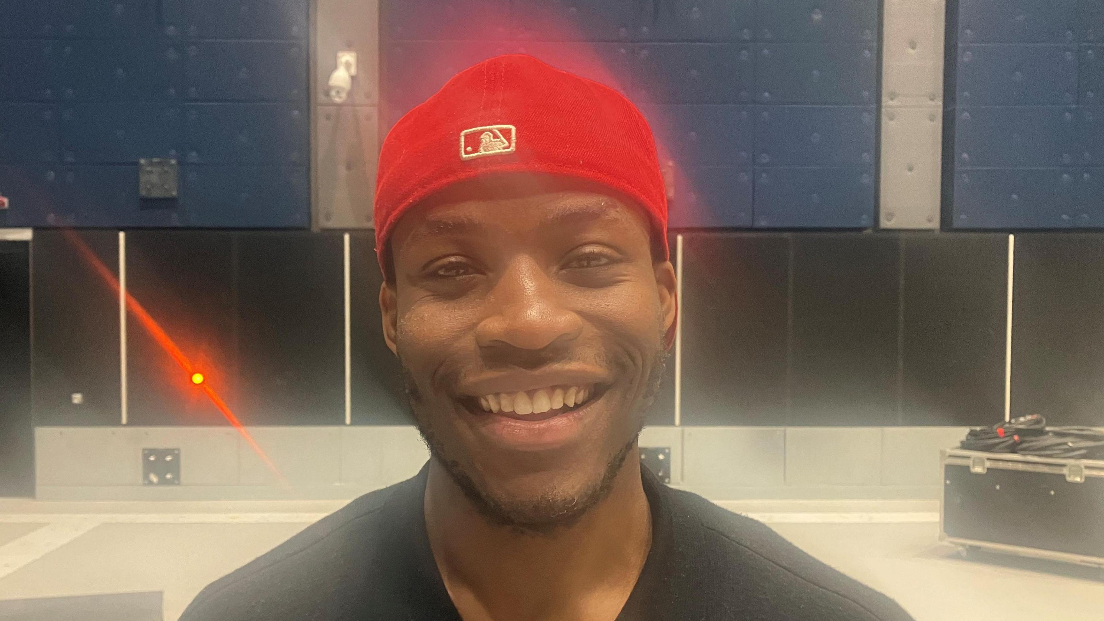 Actor Sean-Marco Msipha wearing a red baseball cap, smiling for the camera at a production space at the Aviva Studios building. 