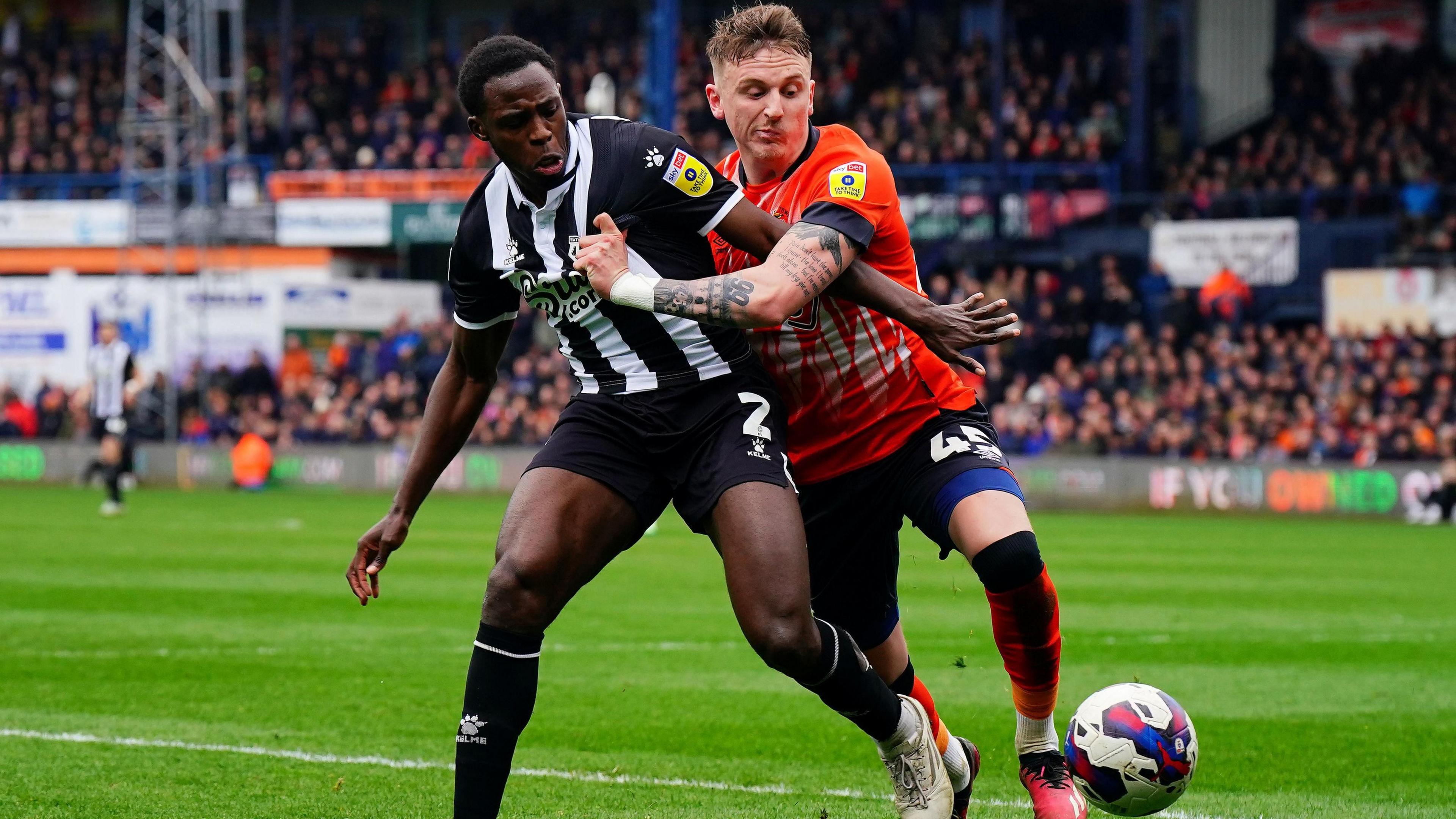 Watford's Jeremy Ngakia (left) in black and white kit and Luton Town's Alfie Doughty, in orange, battle for the ball during a Sky Bet Championship match at Kenilworth Road.