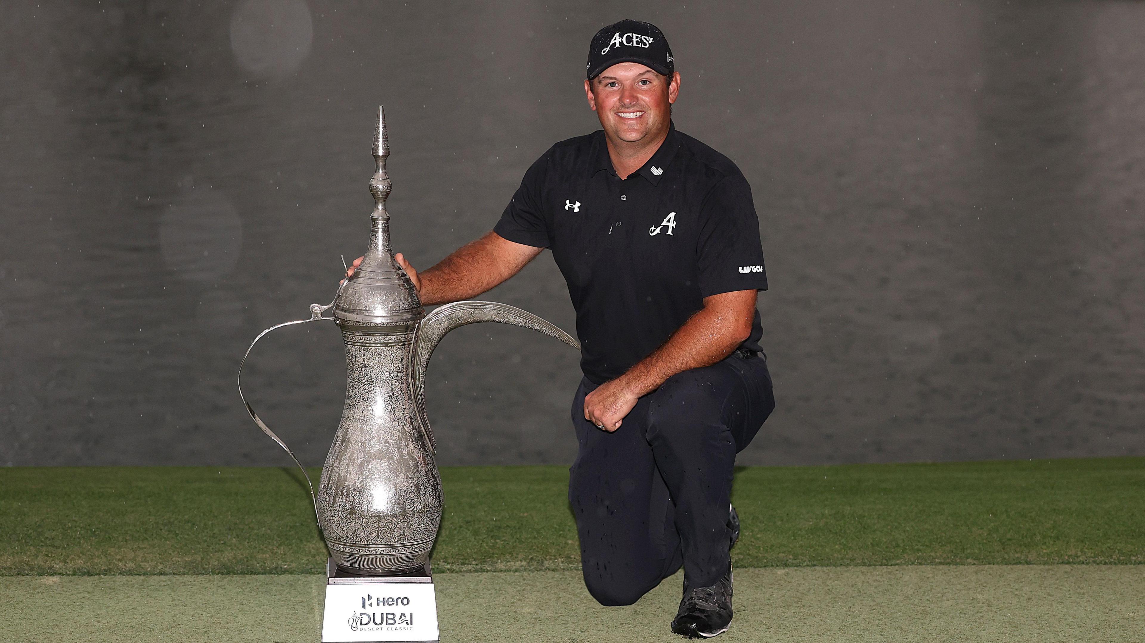 Patrick Reed, dressed in black, kneels down beside the Desert Classic trophy