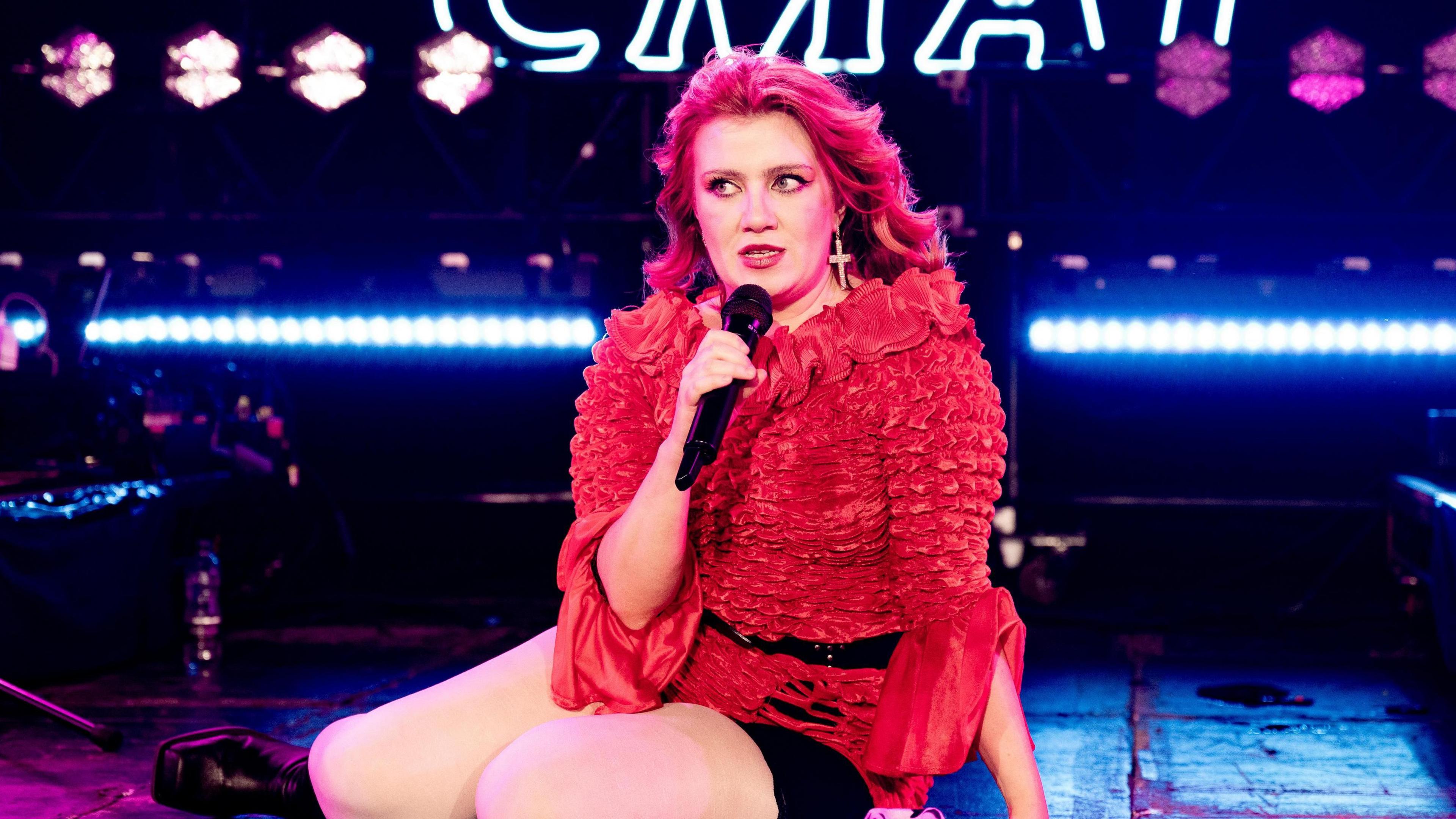 CMAT sits on a stage, singing into a microphone.