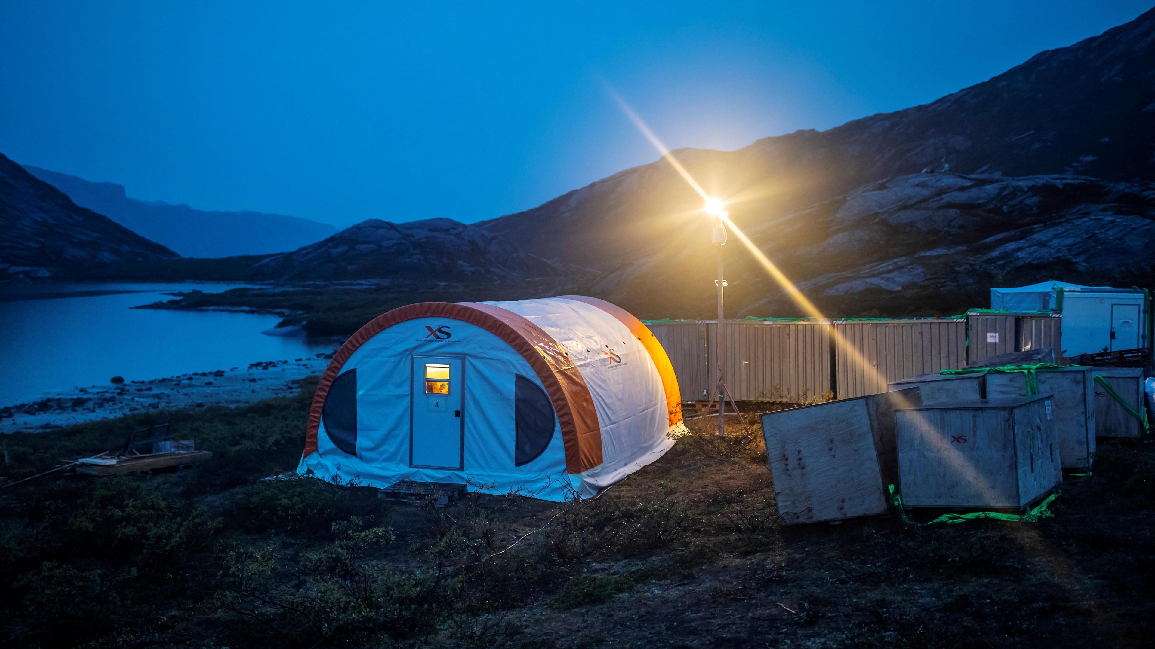 A tent with a bright light above it during twilight at the camp of the exploration site of the company Greenland Anorthosite Mining close to the Qeqertarsuatsiaat fjord, Greenland