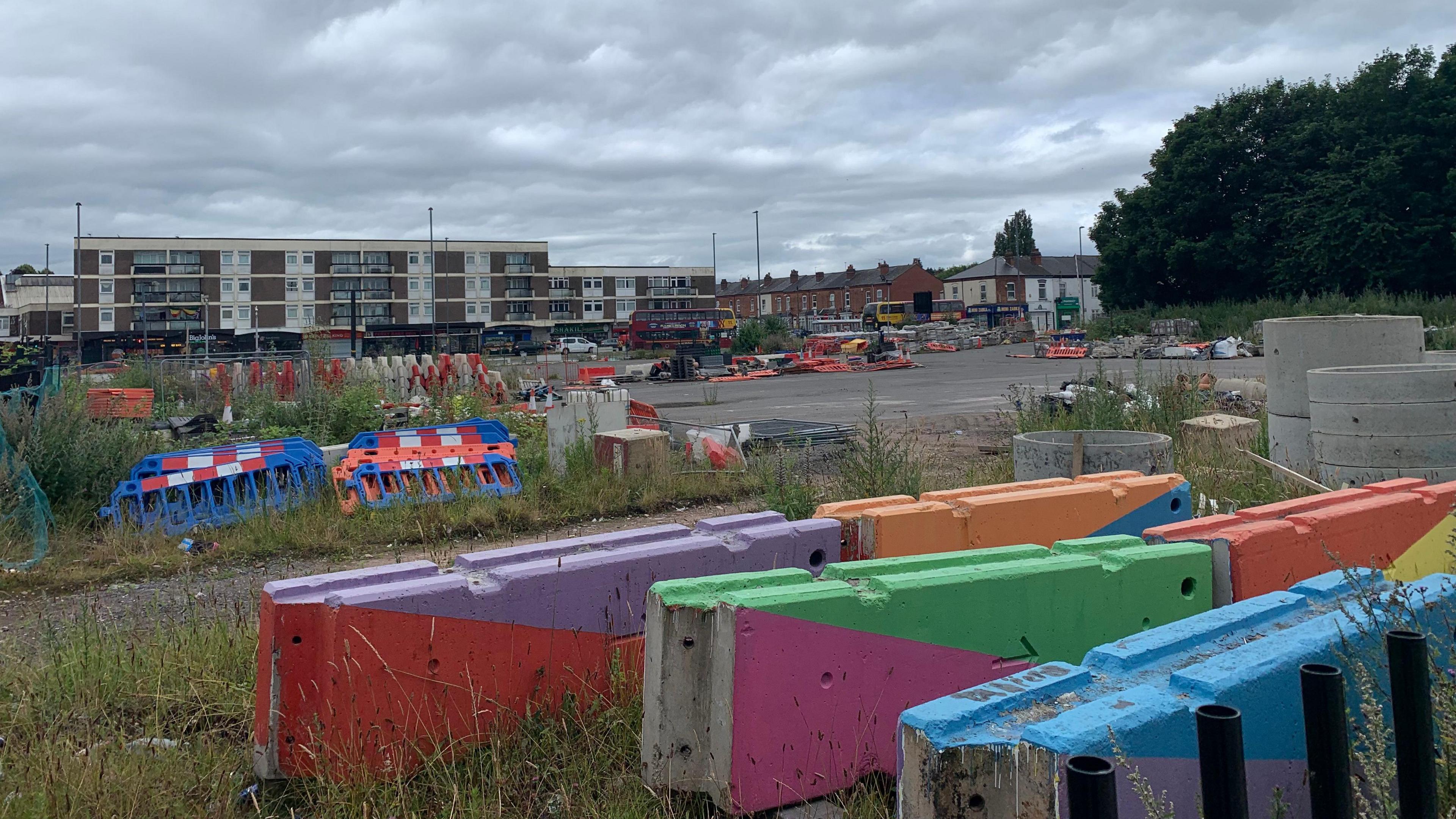 Undeveloped land in Perry Barr. There are concrete blocks with Commonwealth Games colours and it is overgrown with grass and weeds. 