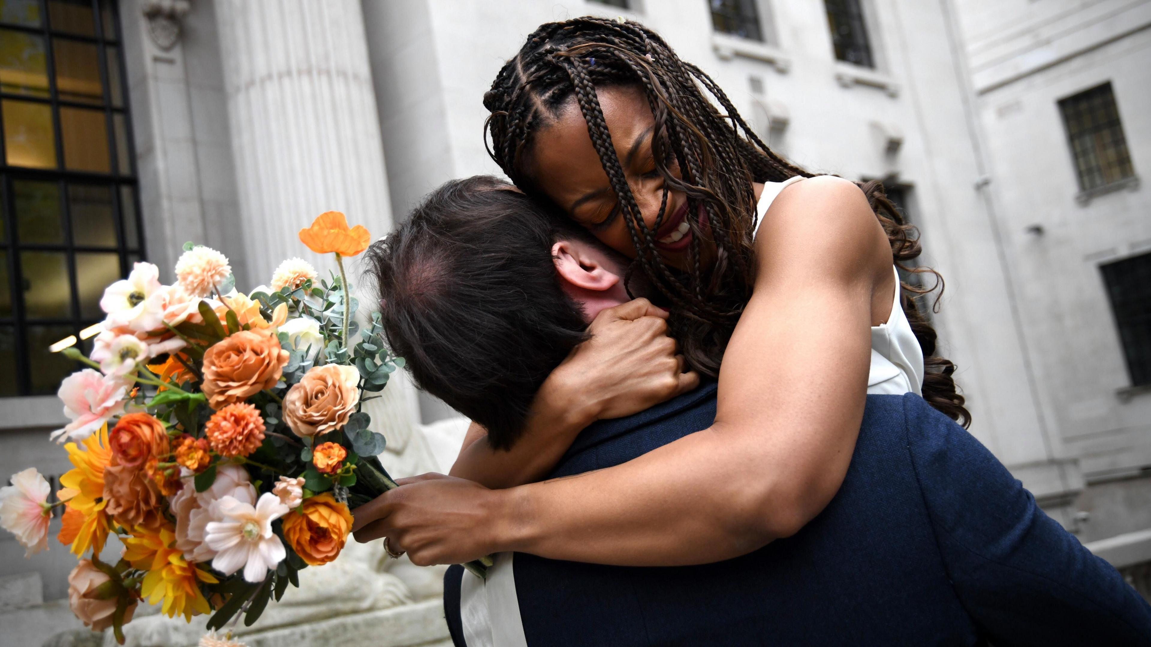 Couple Natasha Whitter and Connor Lynch embrace with a bunch of flowers outside the town hall