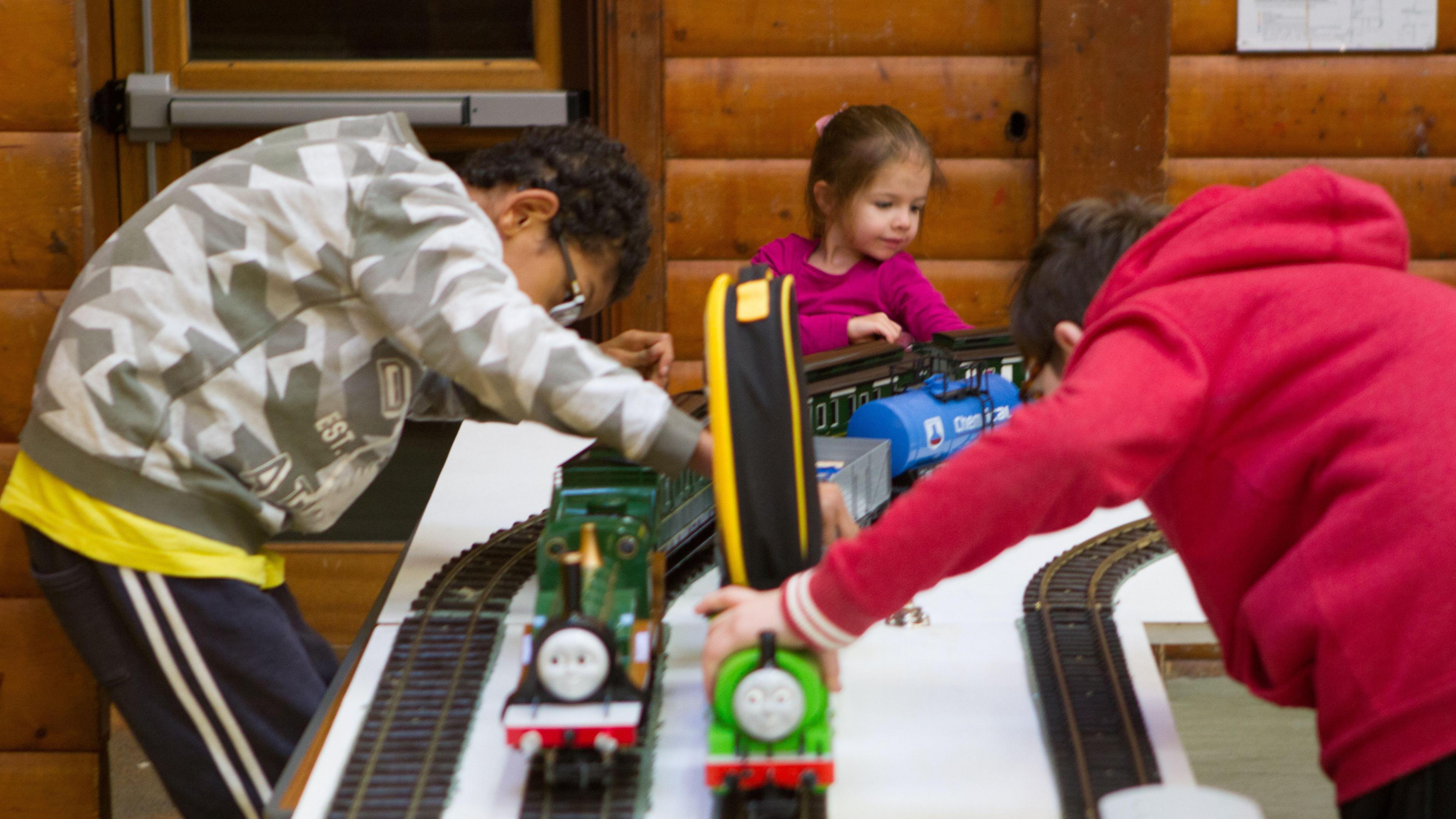 Three children, two boys and one girl all playing with Thomas the Tank engine trains on a toy track
