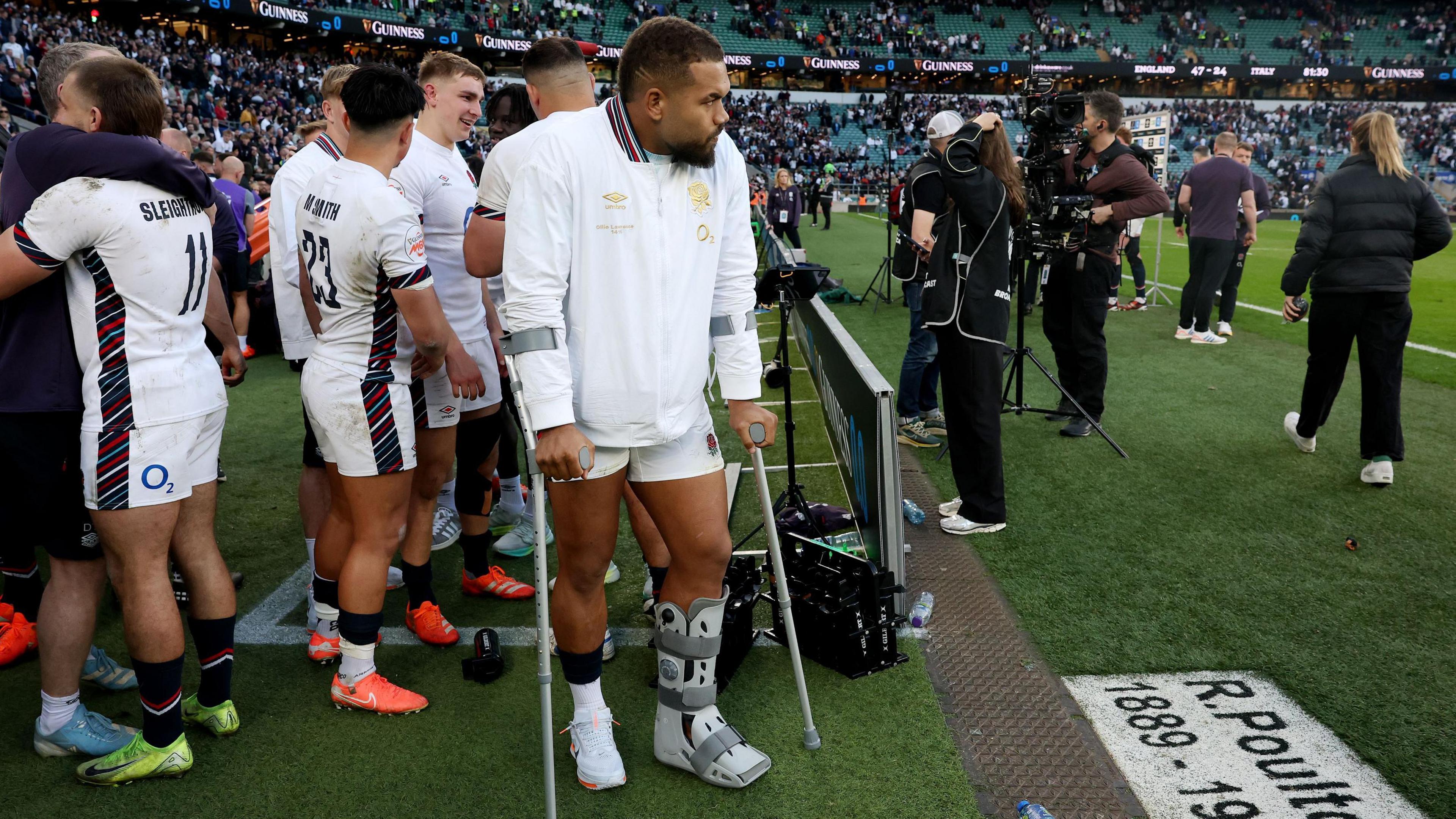 Ollie Lawrence (centre) stands on crutches with his leg in a boot on the sidelines at Twickenham  