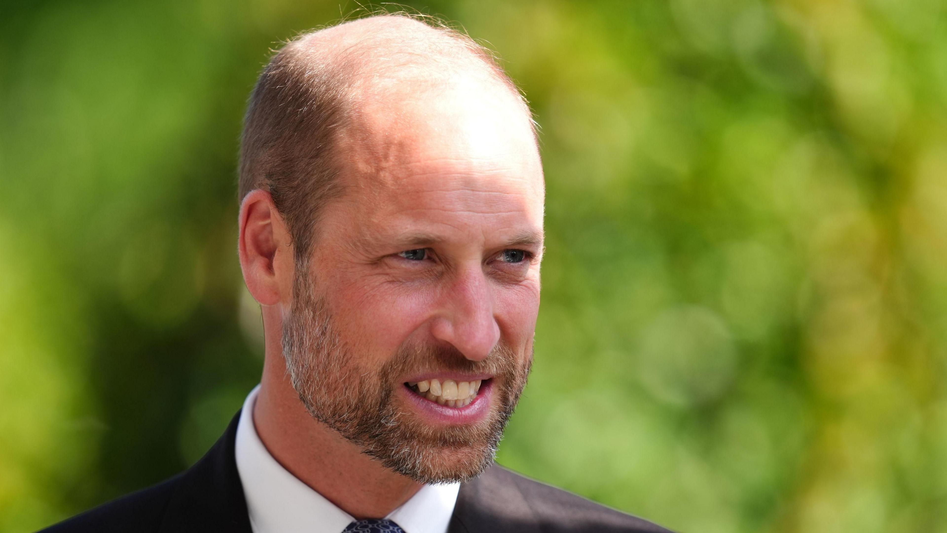 The Prince of Wales smiles against a blurred green background