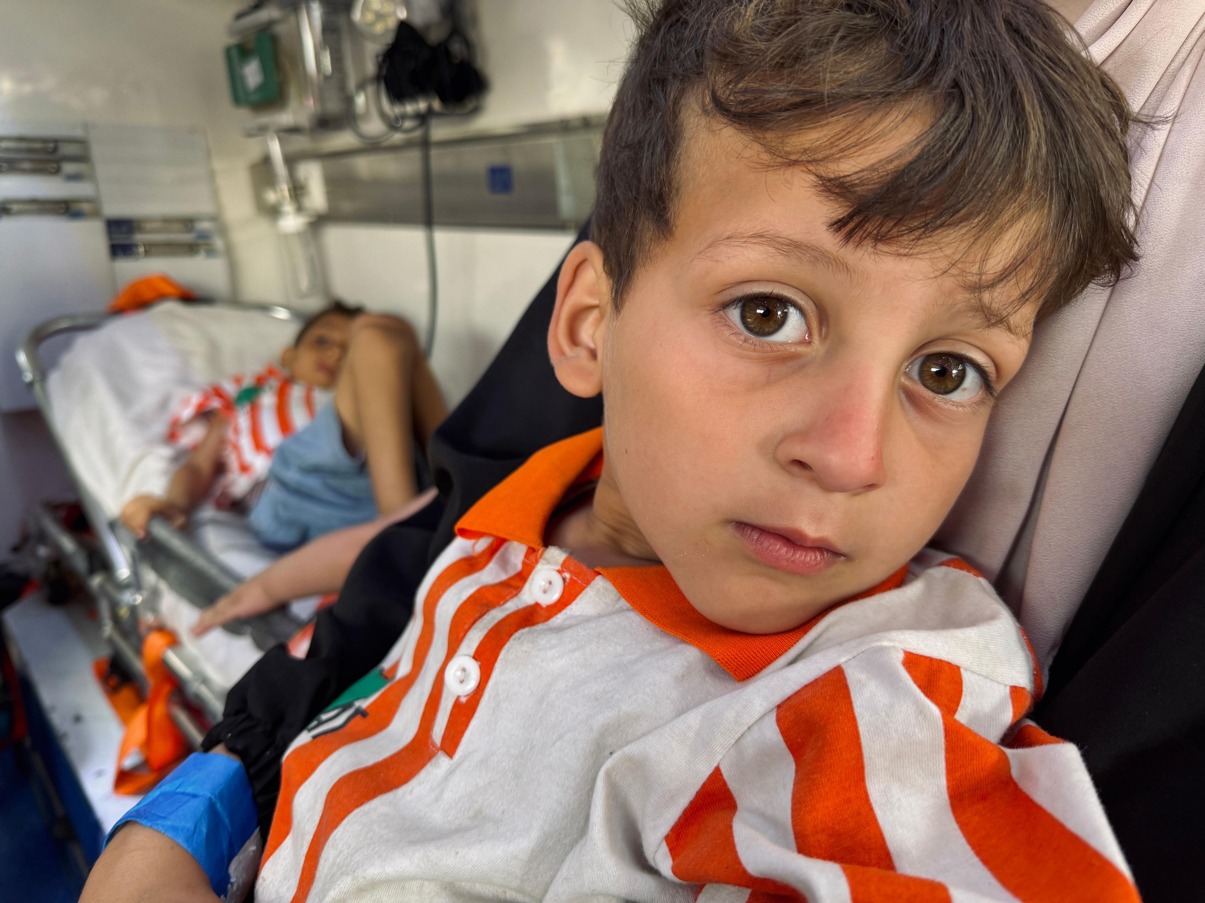 A boy in a red and white shirt sits on the ambulance, with another in a similar shirt lying down behind