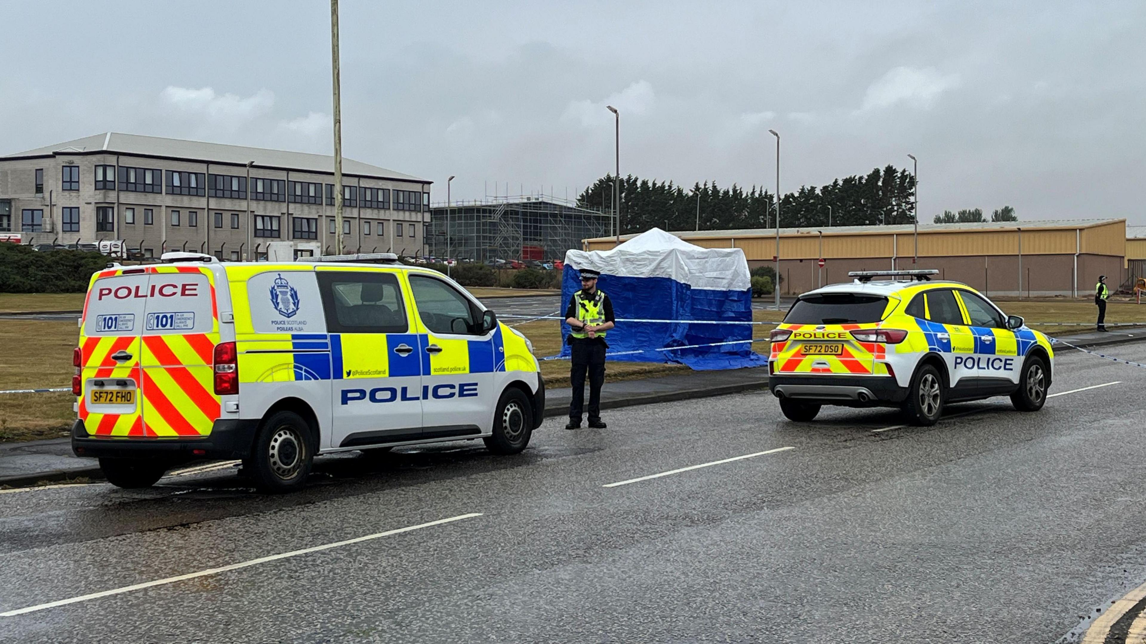 A police van, car and two officers in the road outside an industrial estate