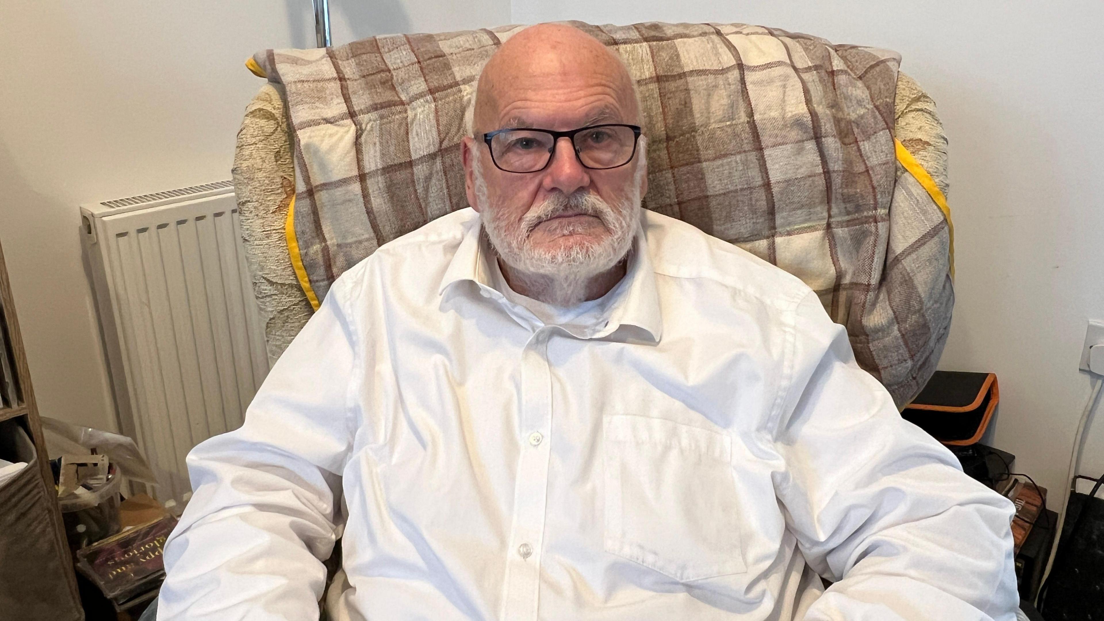 Eastfield town councillor Kenneth Elbourne is sitting in an armchair looking straight at the camera. He is wearing a white shirt, spectacles and has a neatly-trimmed beard.