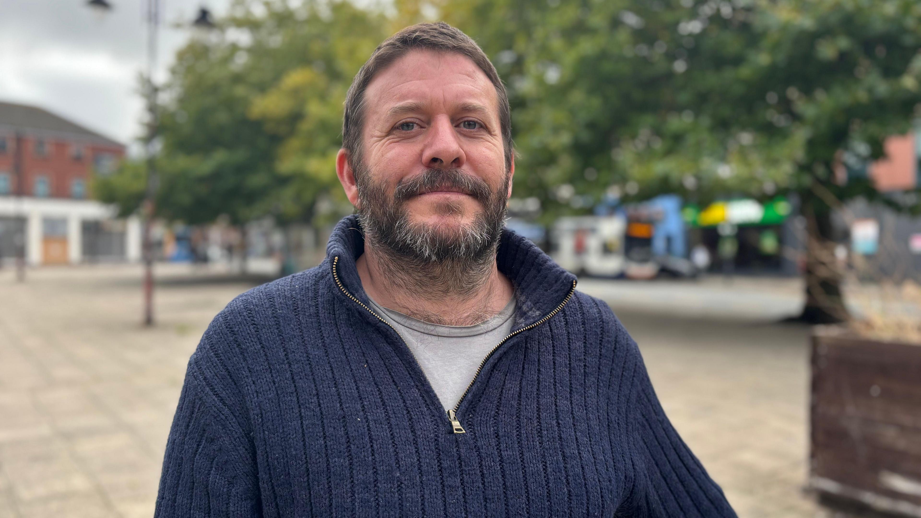 Ed Gommon, who has short dark brown hair and a beard, smiles at the camera while wearing a blue half-zip fleece.