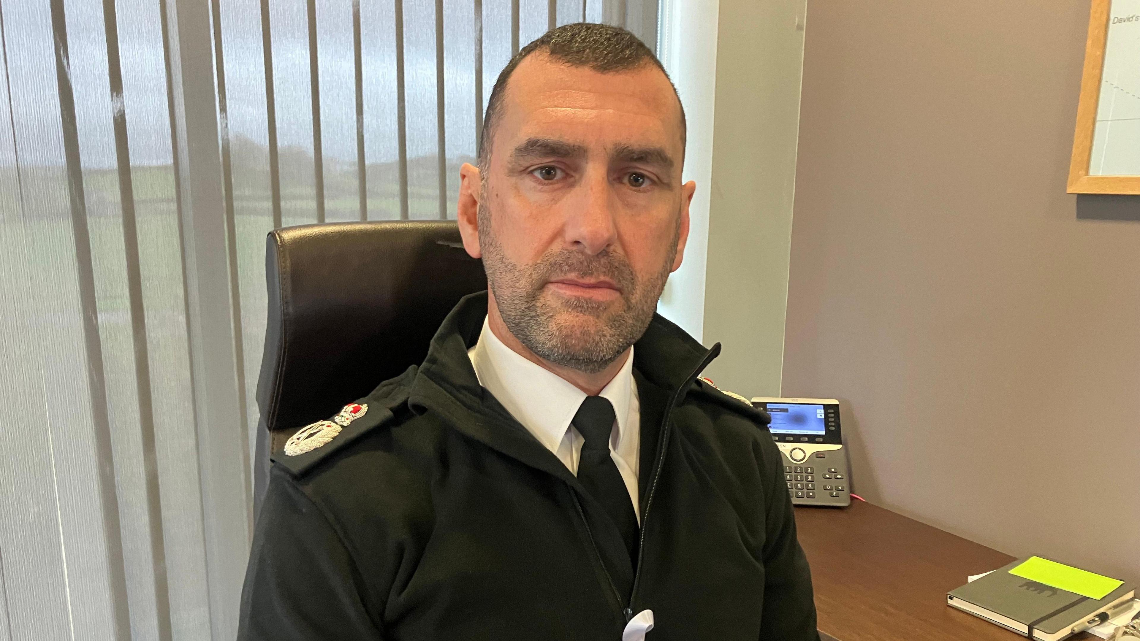 Dr Richard Lewis who is wearing police uniform and is sat beside a desk 