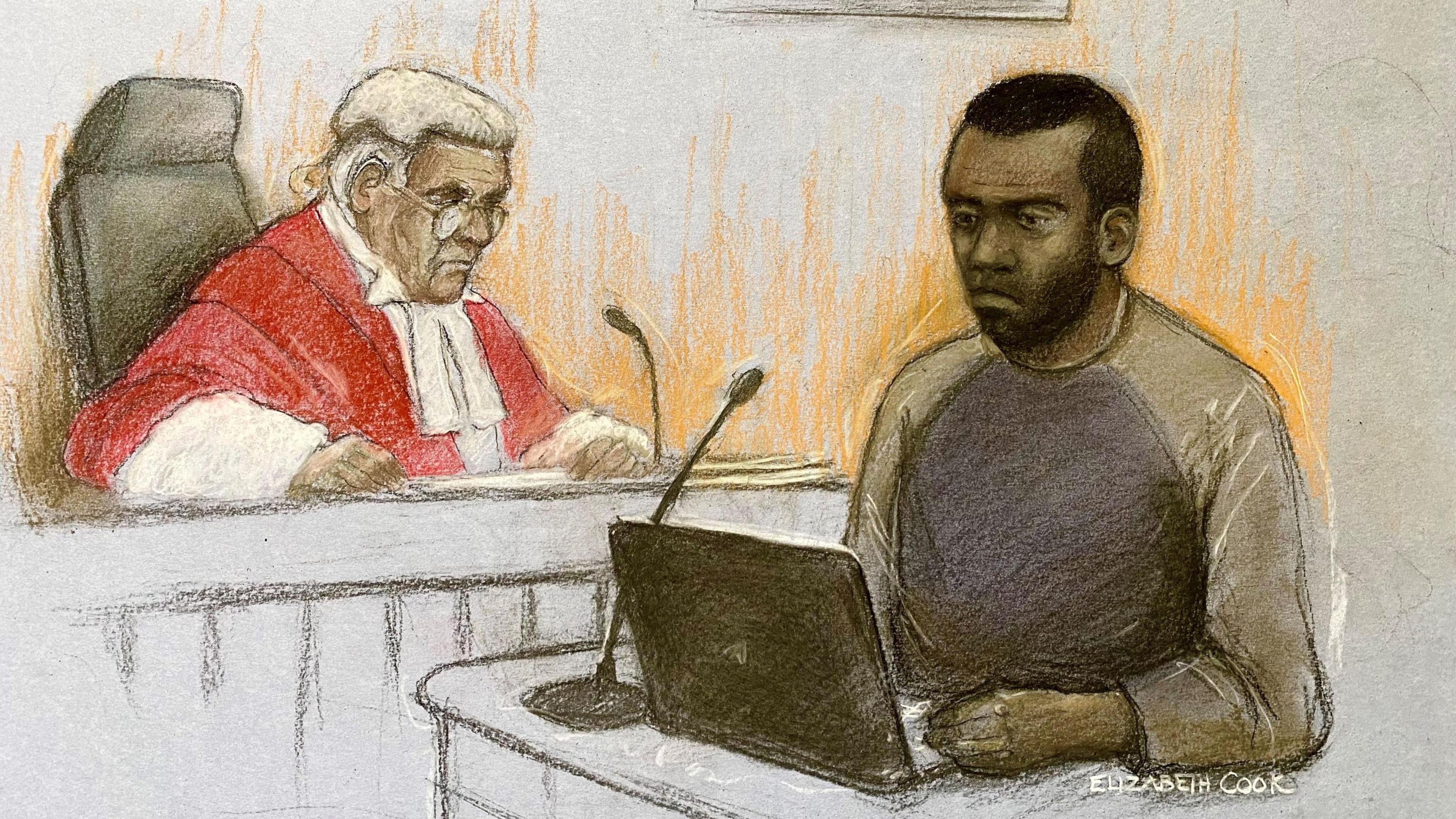 A sketch of the defendant standing in front of a laptop and microphone, with dark hair and facial hair, wearing a blue and grey top. A judge is to the left of him, looking over. He has a white wig on, red robed with white details and glasses.