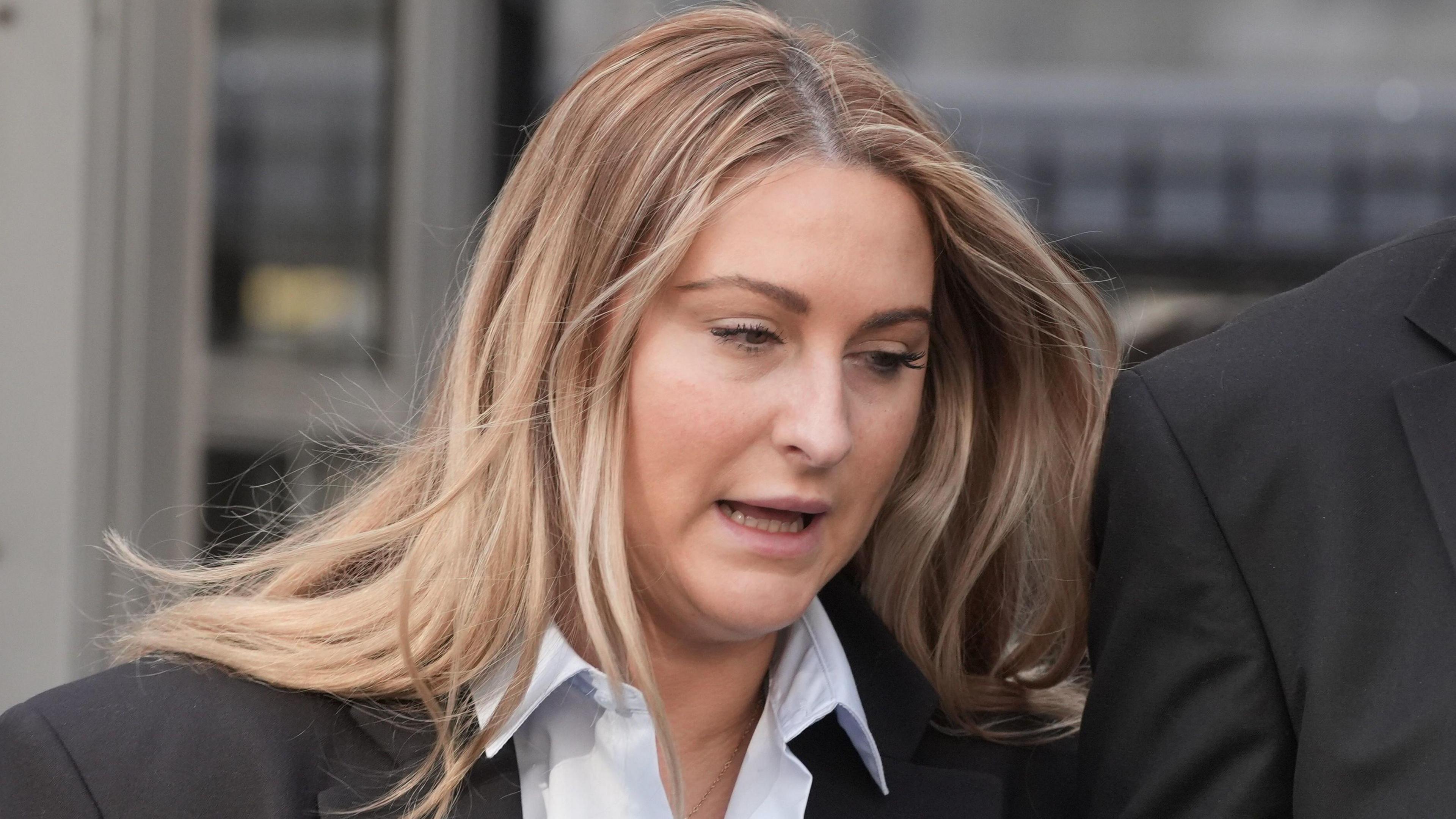 A blonde women wears a black suit and white shirt