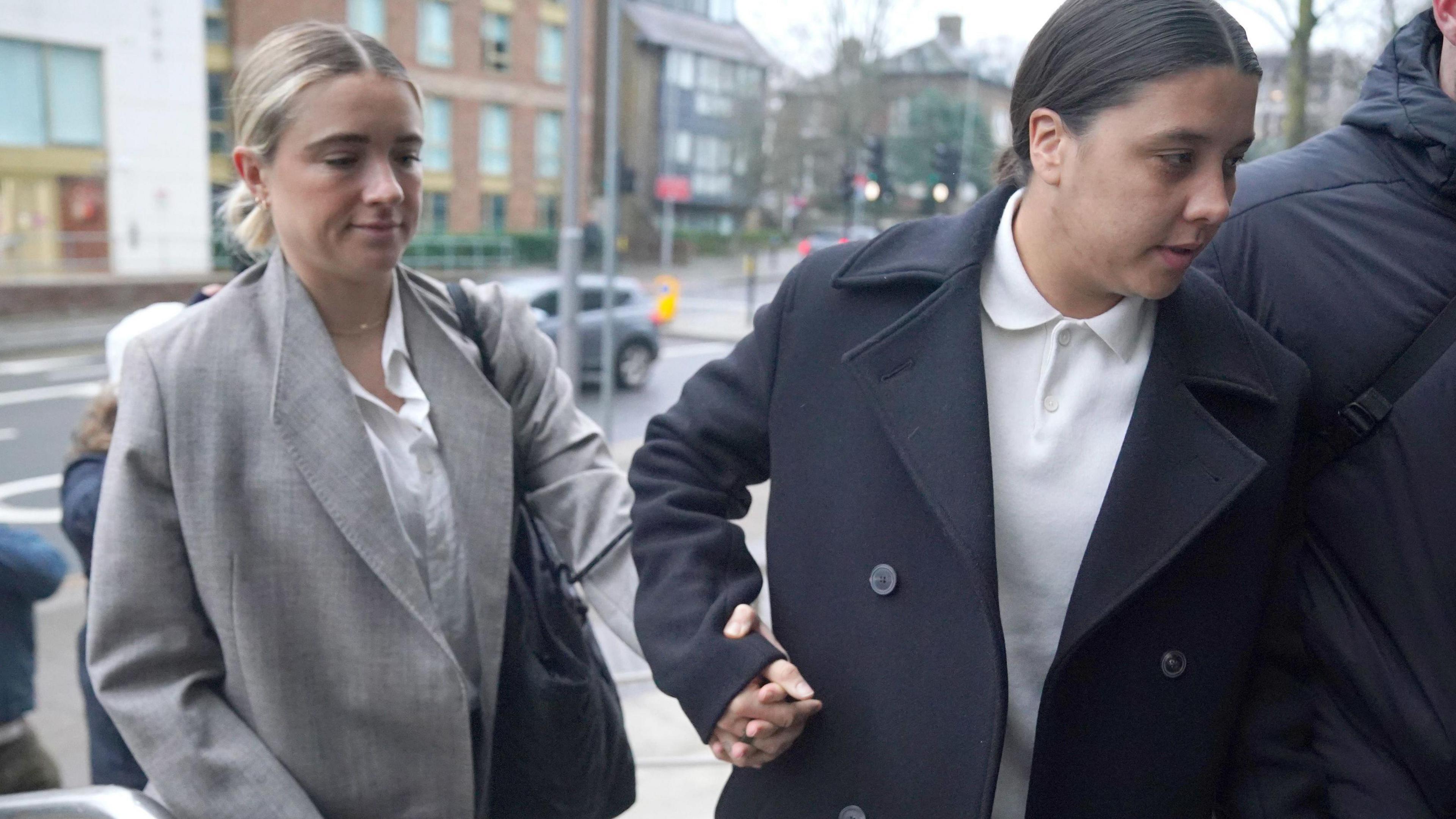 Kristie Mewis and Sam Kerr holding hands and arriving at court. Both are dressed smartly.