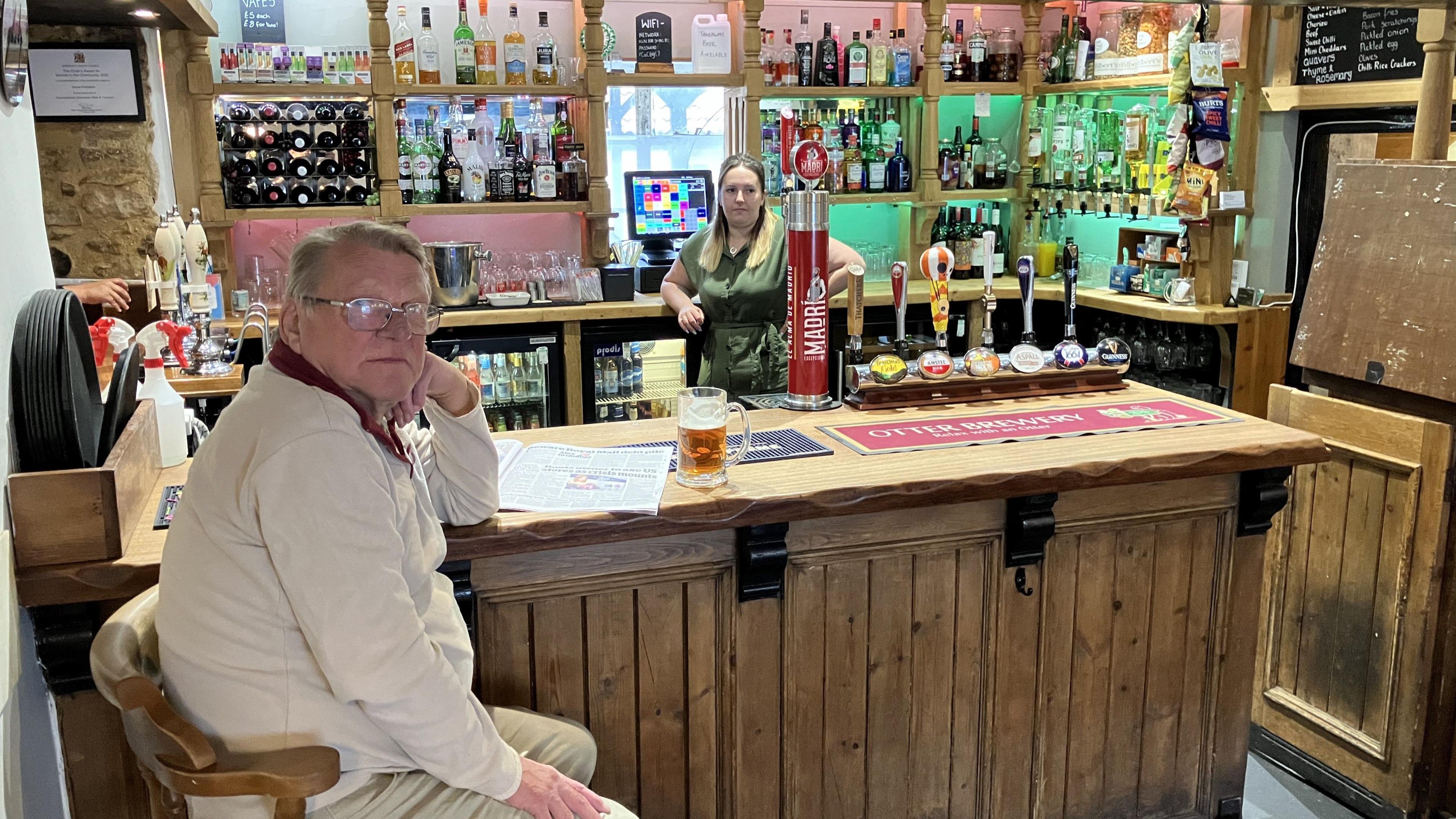 Bill sat at the bar with a pint in a tankard, while Gemma stands behind the bar