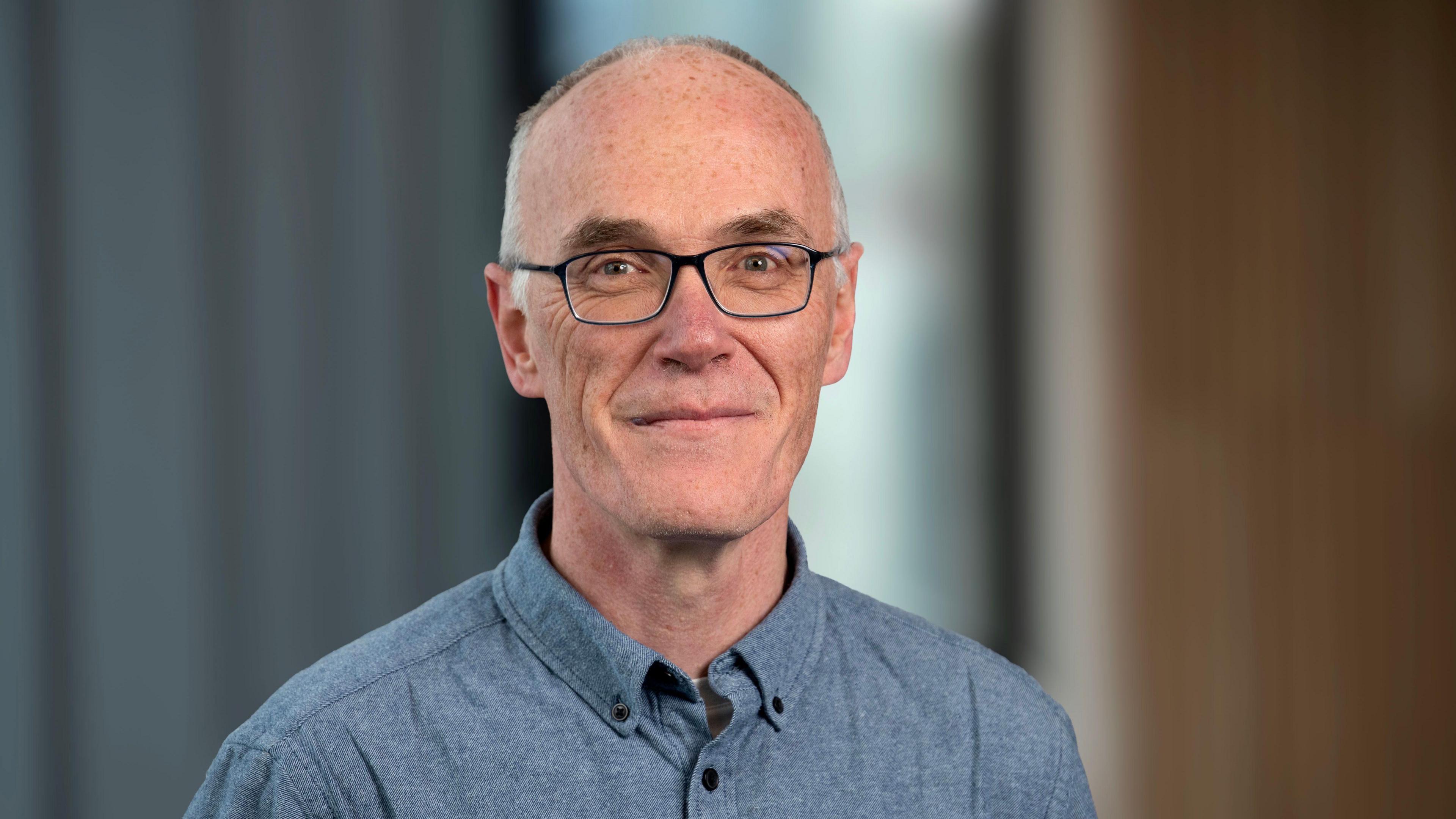 Dr Eoin Magennis, a bald man wearing glasses and a blue shirt