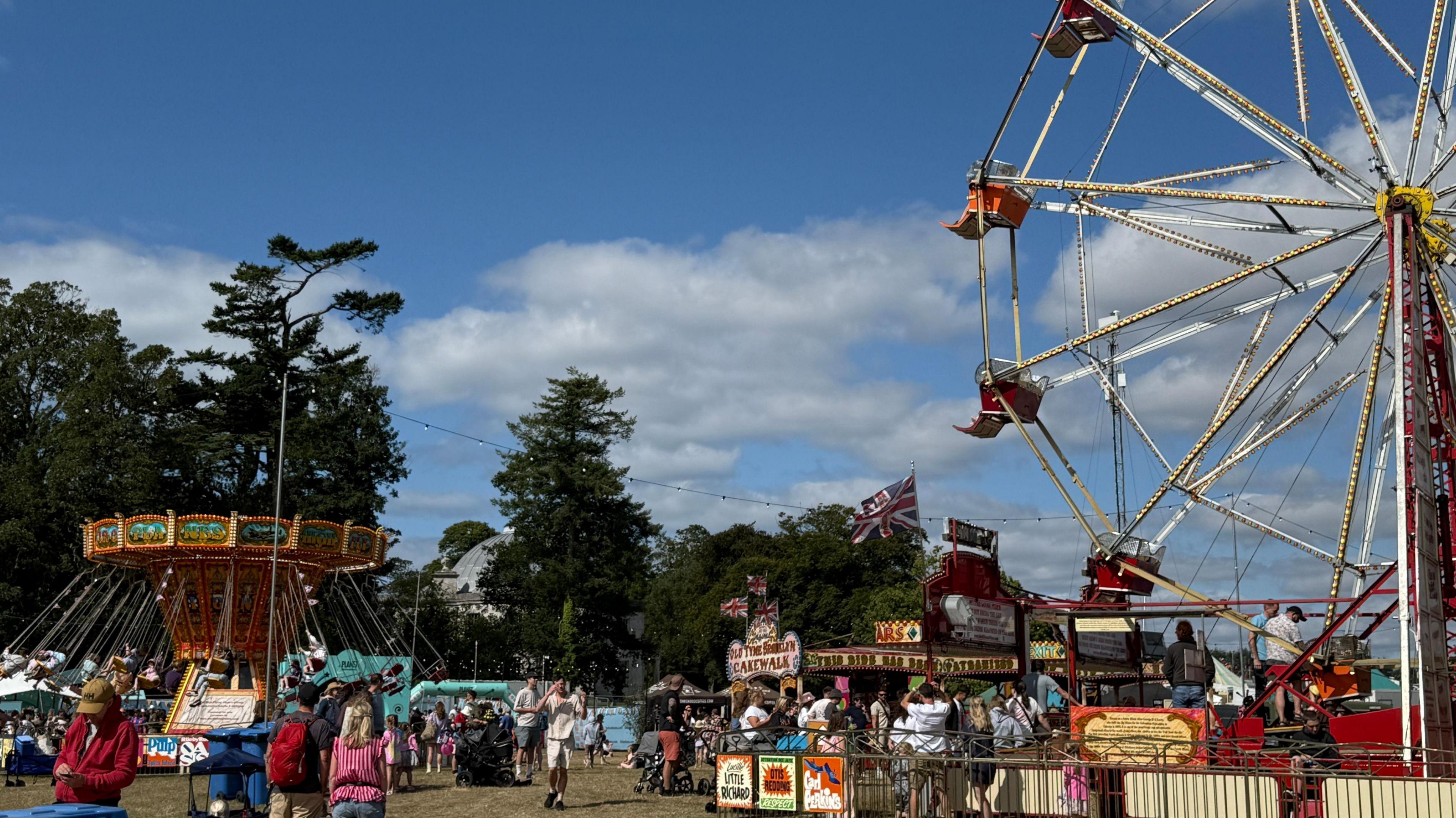 A Ferris wheel goes around as people mill around it.