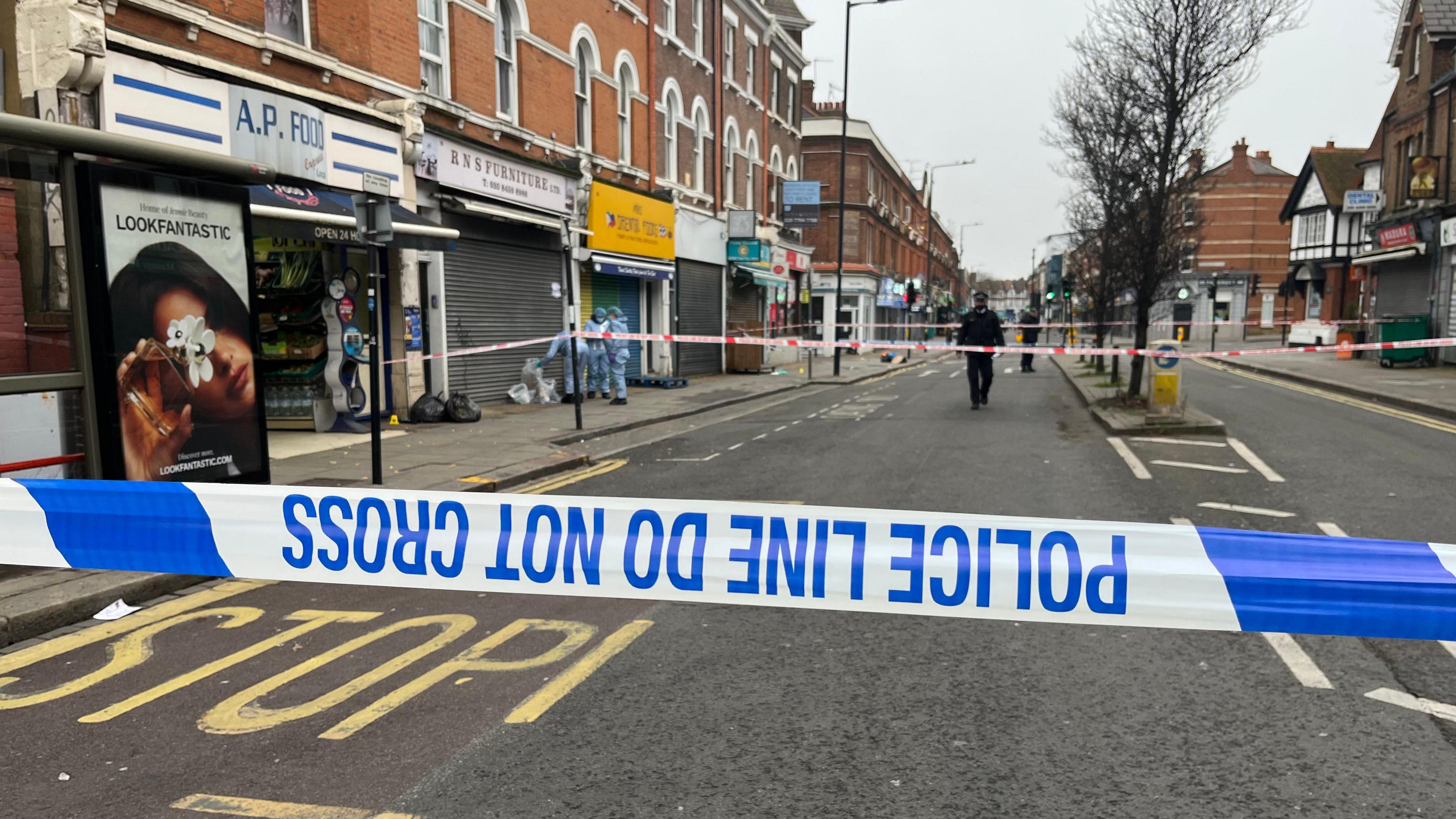 Police cordon tape on a London road. A police officer is seen in the distance.