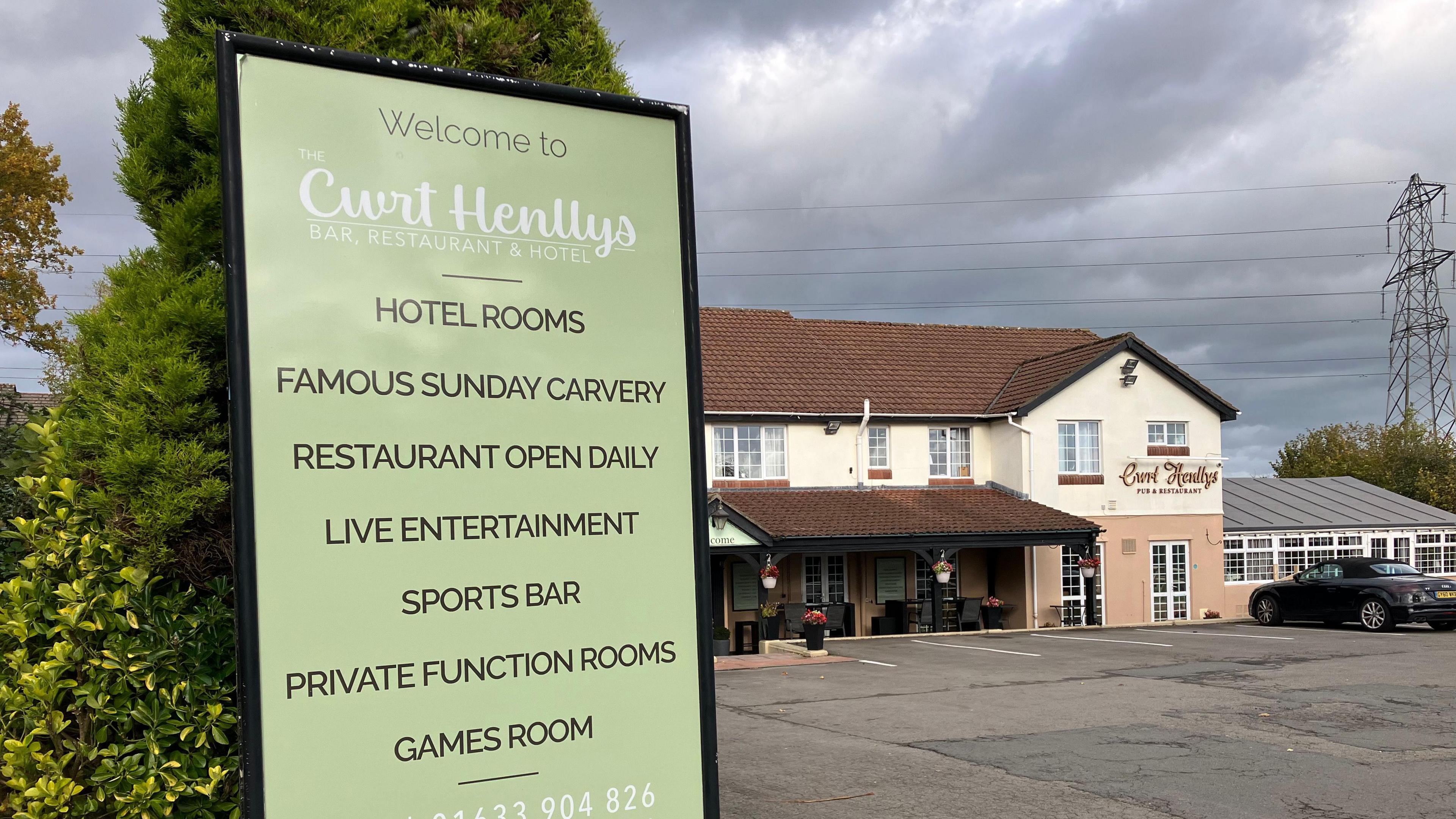 Cwrt Henllys Bar & Restaurant, a two-storey building painted cream and peach, with a red tile roof. A tarmac carpark is at the front of the building. A sign advertises a "famous Sunday carvery"