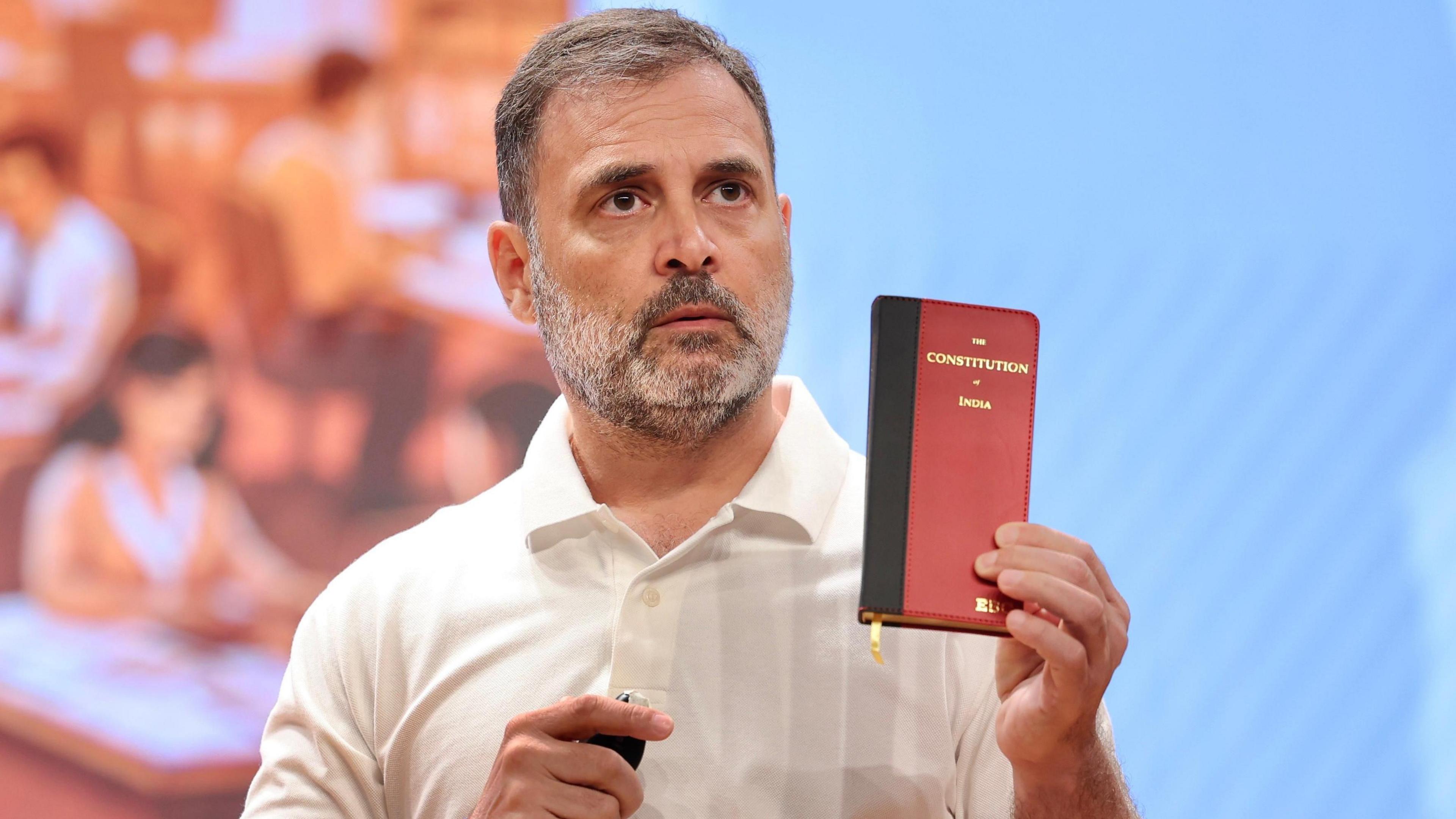 Rahul Gandhi, wearing a white T-shirt, holds up a copy of India's constitution