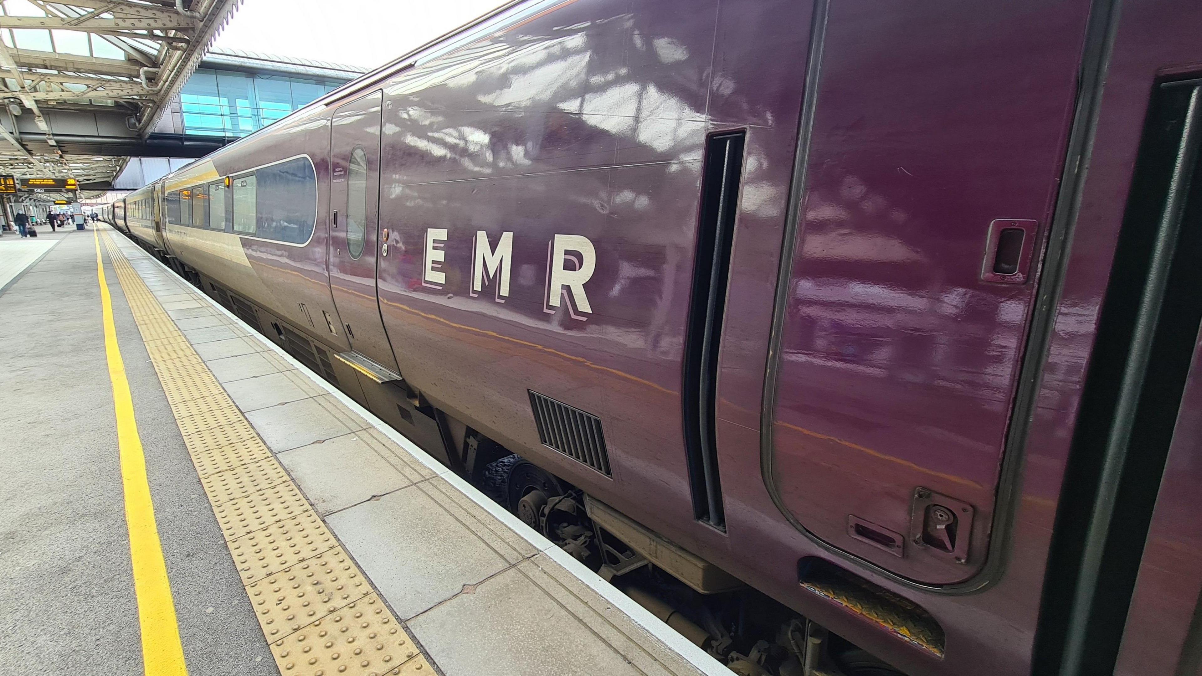 An EMR train in purple livery next to a train station stop