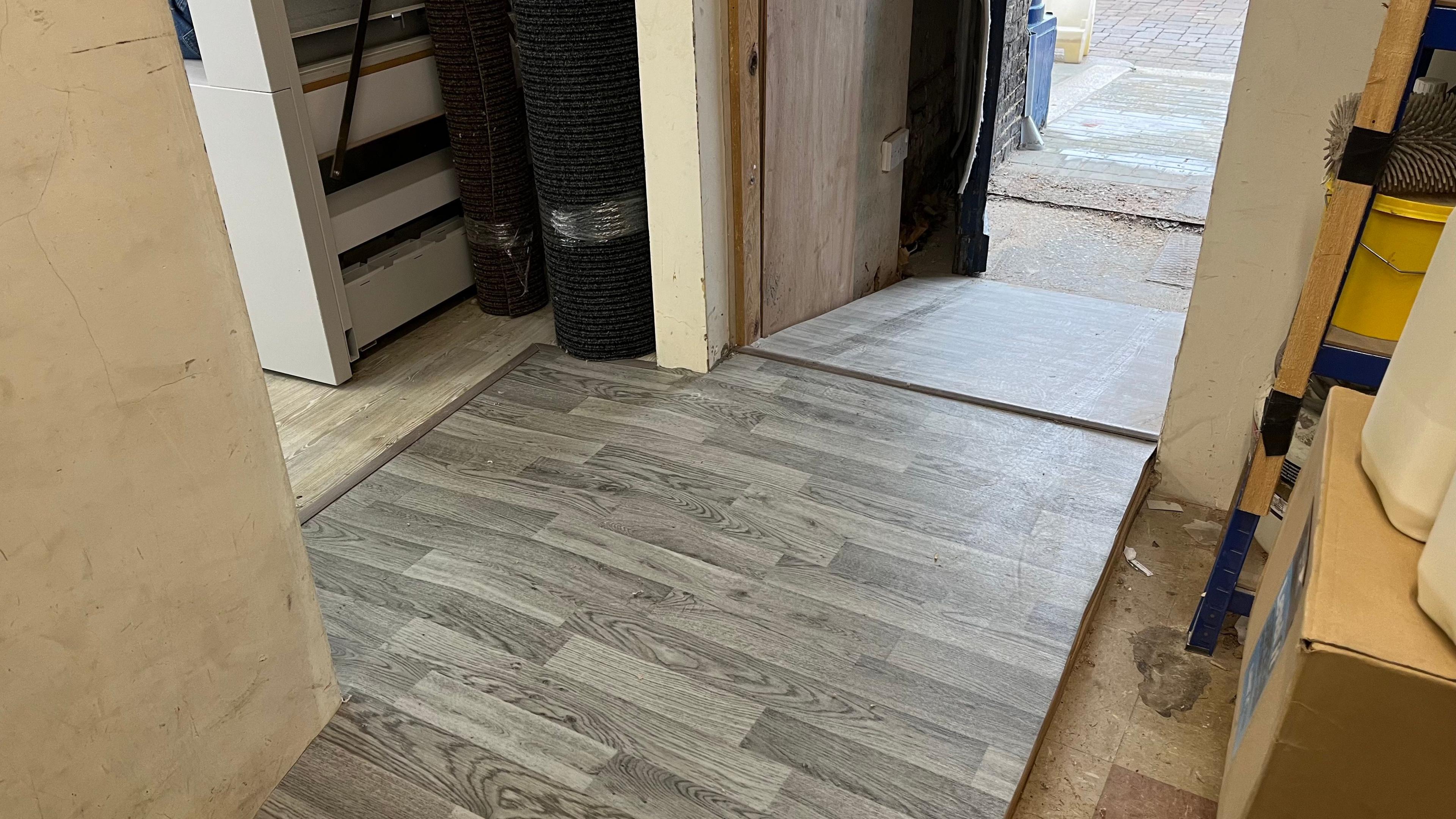 A ramp with grey laminate flooring which leads to a doorway and outside the FBI shop.