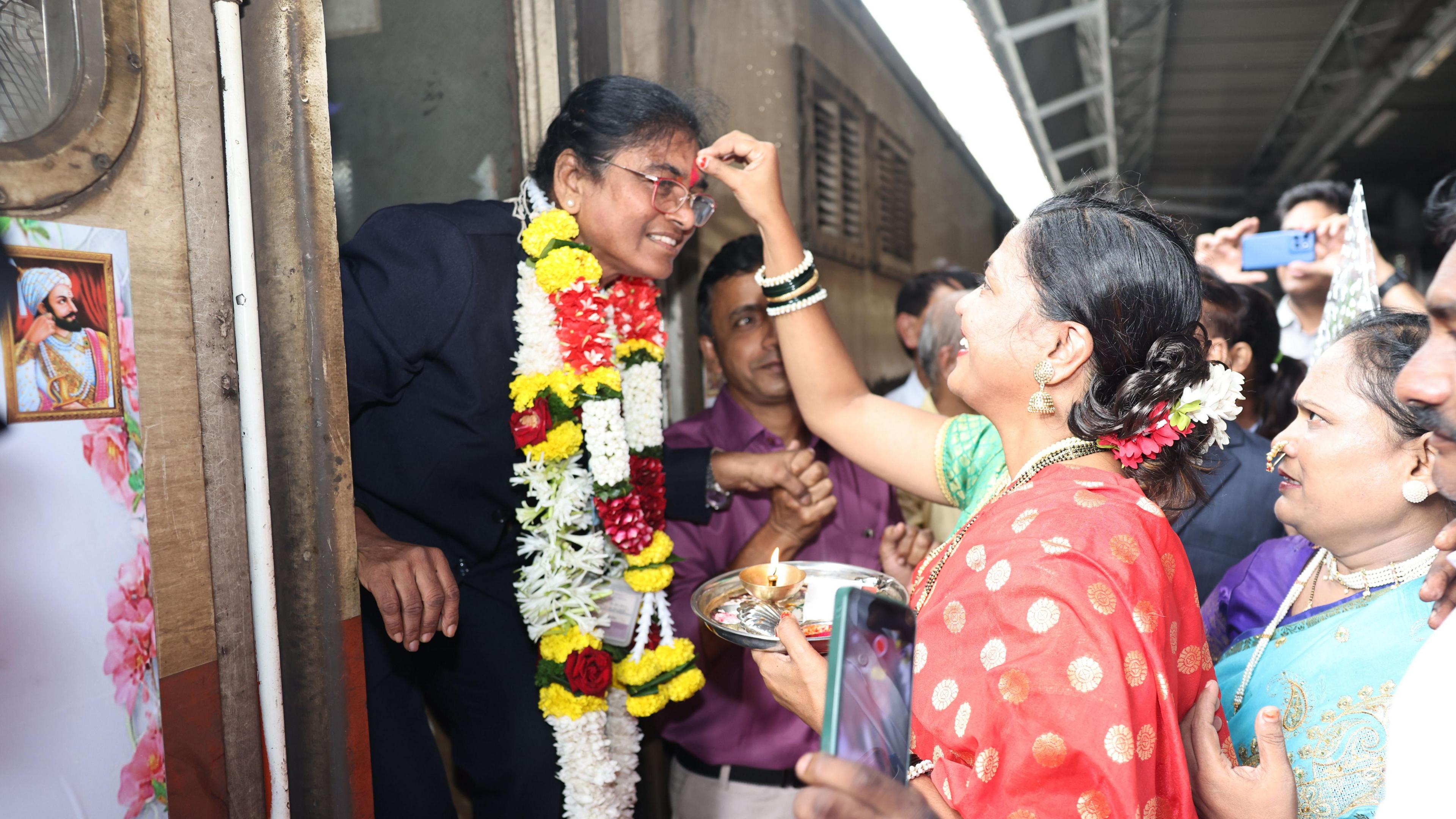 A lady dressed in a sari applies red powder of Ms Yadav's forehead as she exits a train in Mumbai, India.