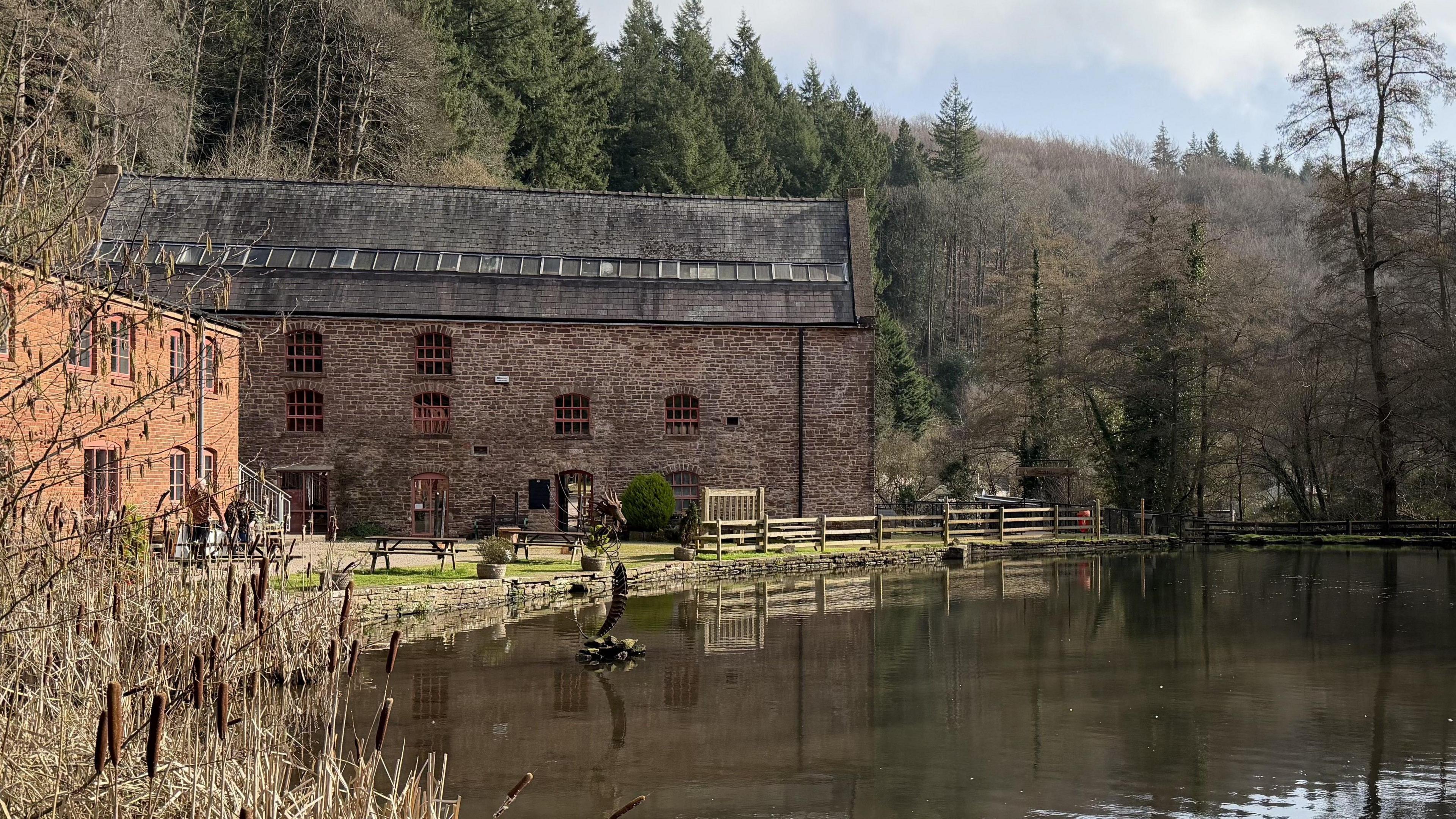 A photo of Soudley Ponds in the Forest of Dean. It shows a building surrounded by trees next to a pond