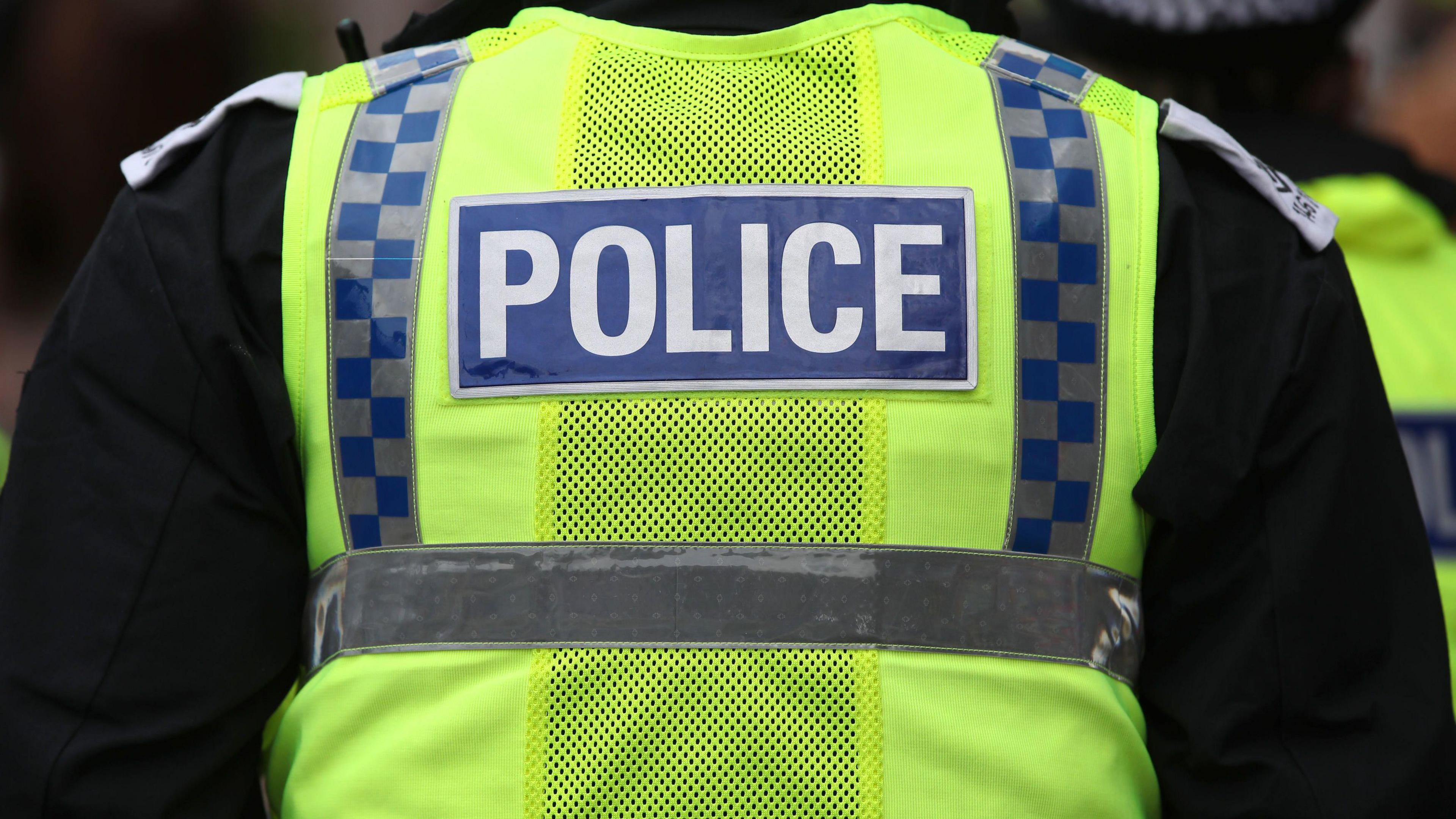 Image of a police officer. He is wearing a high vis vest with police written across the back