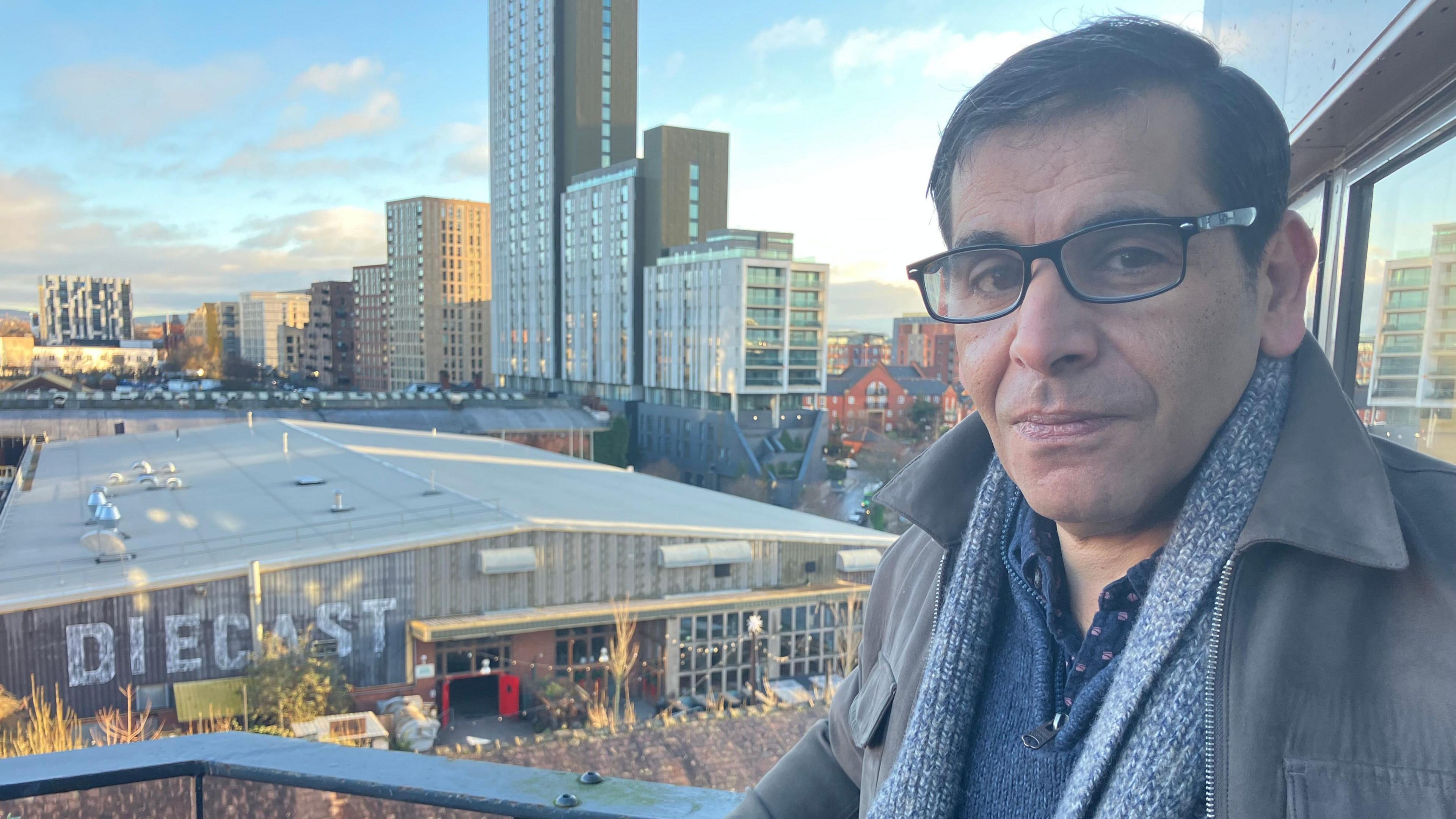 Maged Selim leans on a balcony from his apartment looking over the flat-roofed former steelworkers across the street which has been converted into a multi-use events space.