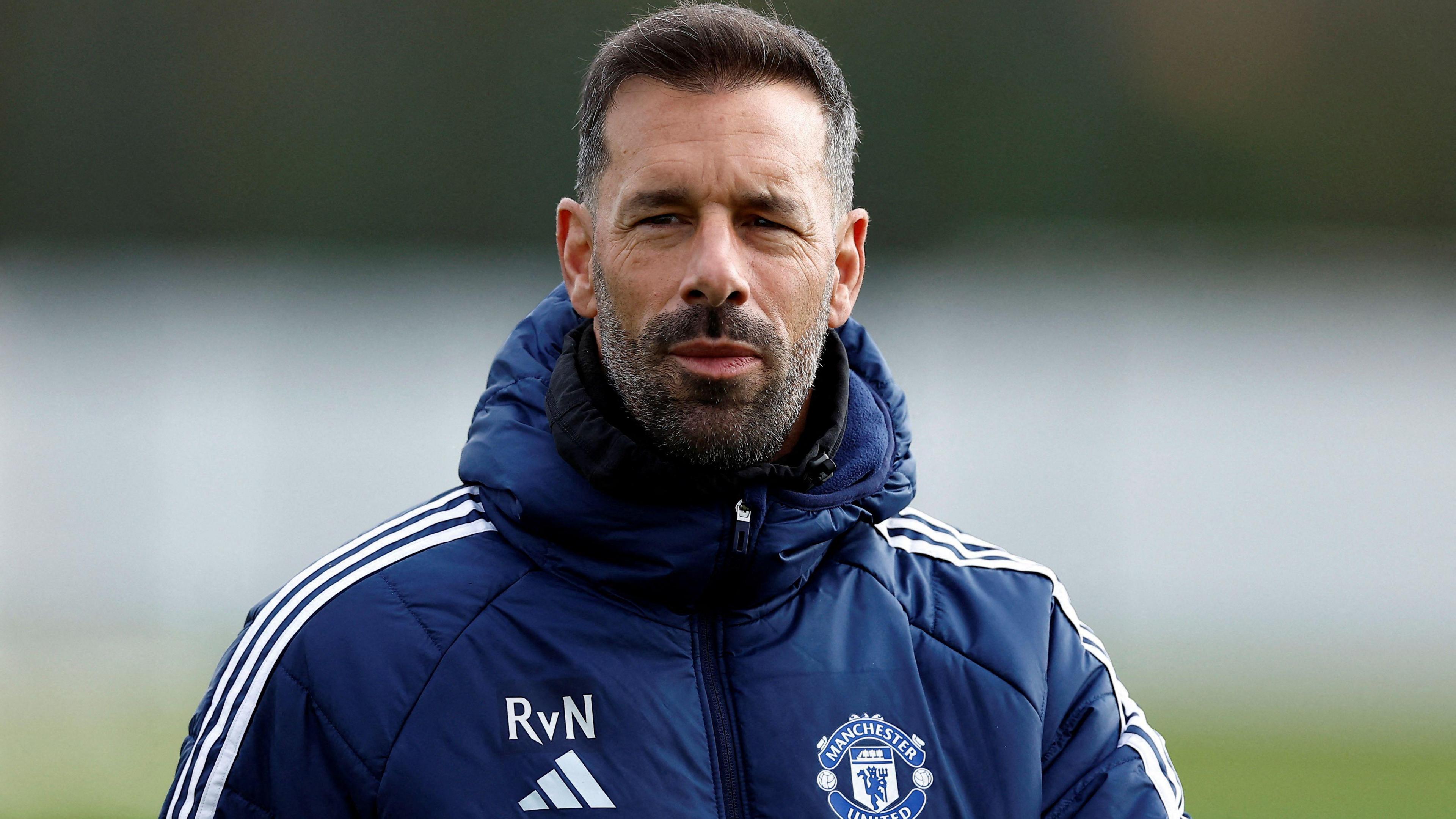 The image shows interim manager Ruud van Nistelrooy wearing a navy coat 