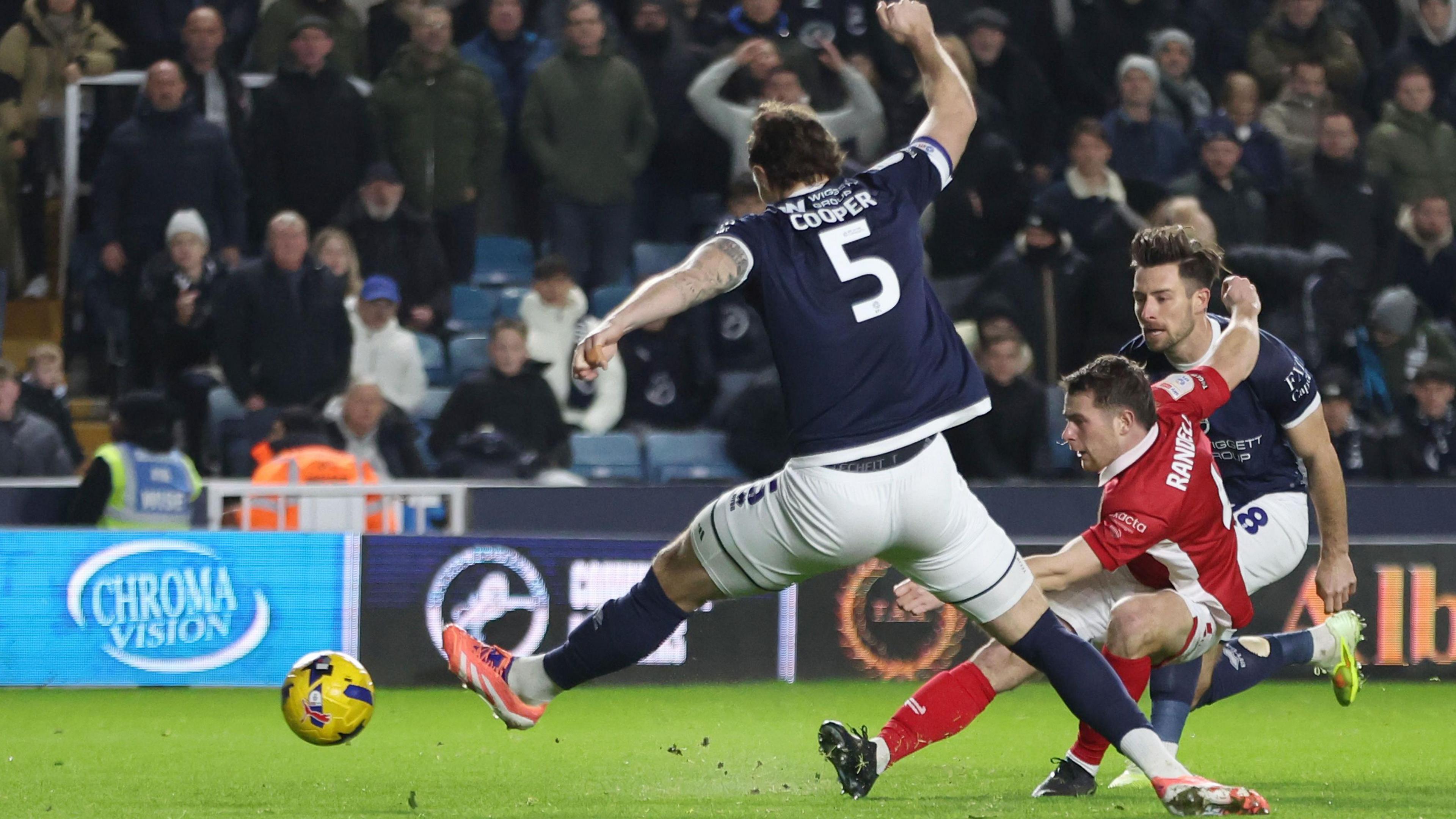 Adam Randell shoots the ball between Millwall captain Jake Cooper's legs