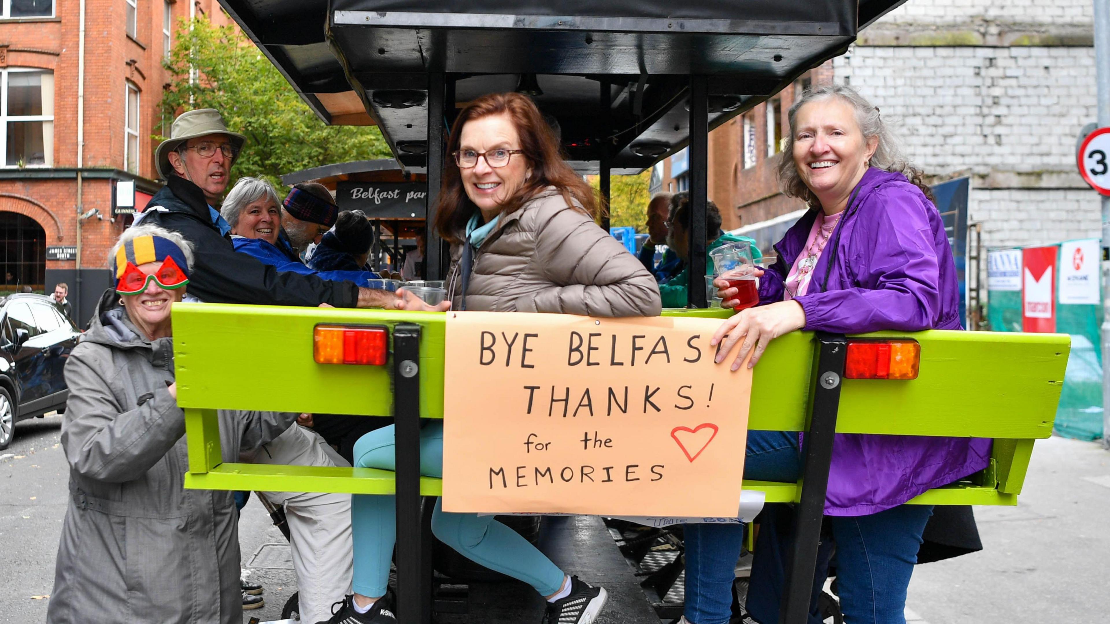 Passengers of the cruise ship smiling on a beer bike in Belfast with a sign that says 'Bye Belfast, thanks for the memories'