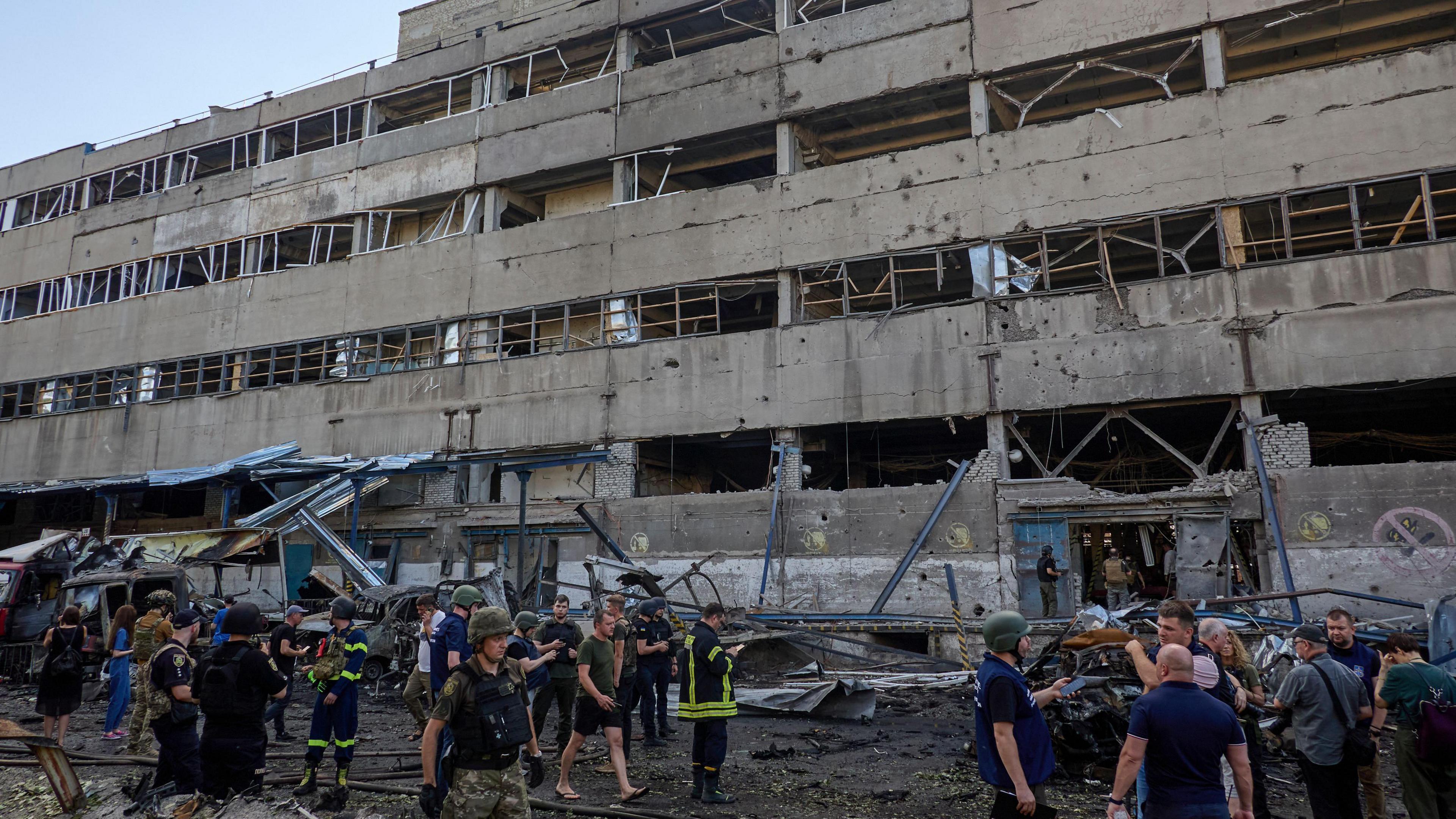 A grey building with no windows and emergency workers and others round the outside.