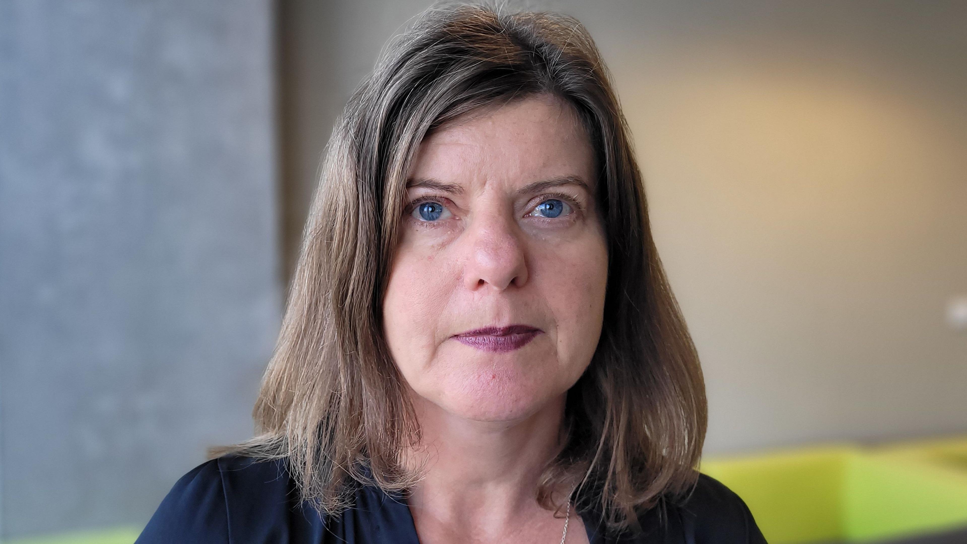 Sandy Brindley, who has blue eyes, sandy-coloured hair in a long bob, and purple lipstick, looks into the camera.