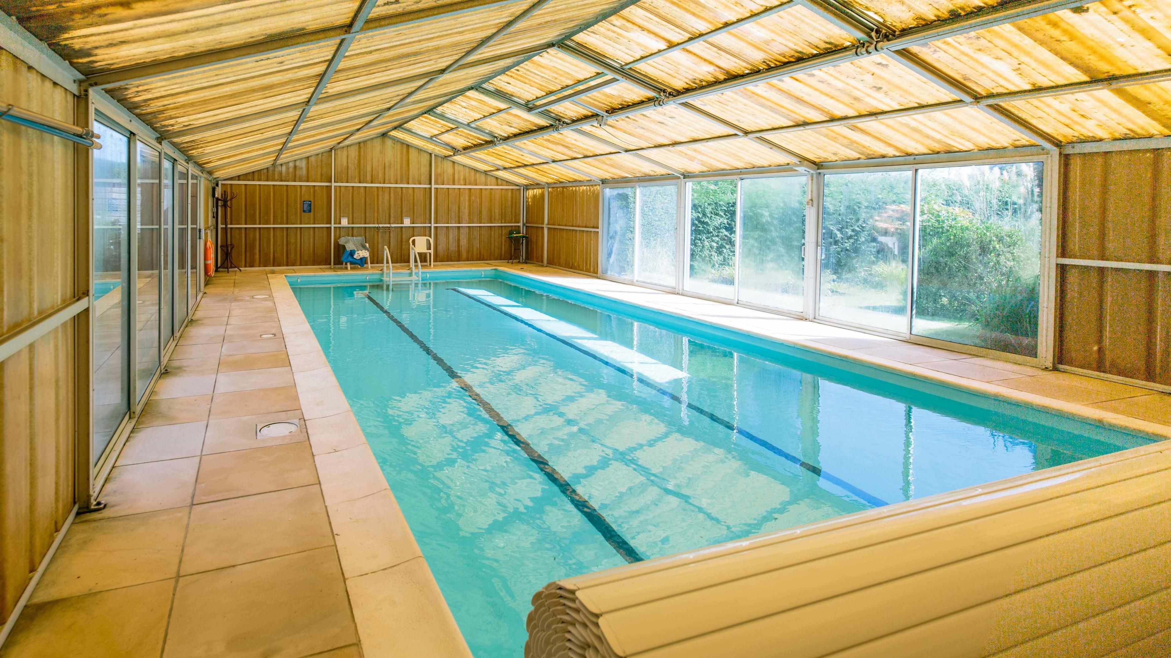 A swimming pool with three lanes. It is within a building that has yellow walls and roof and large windows.