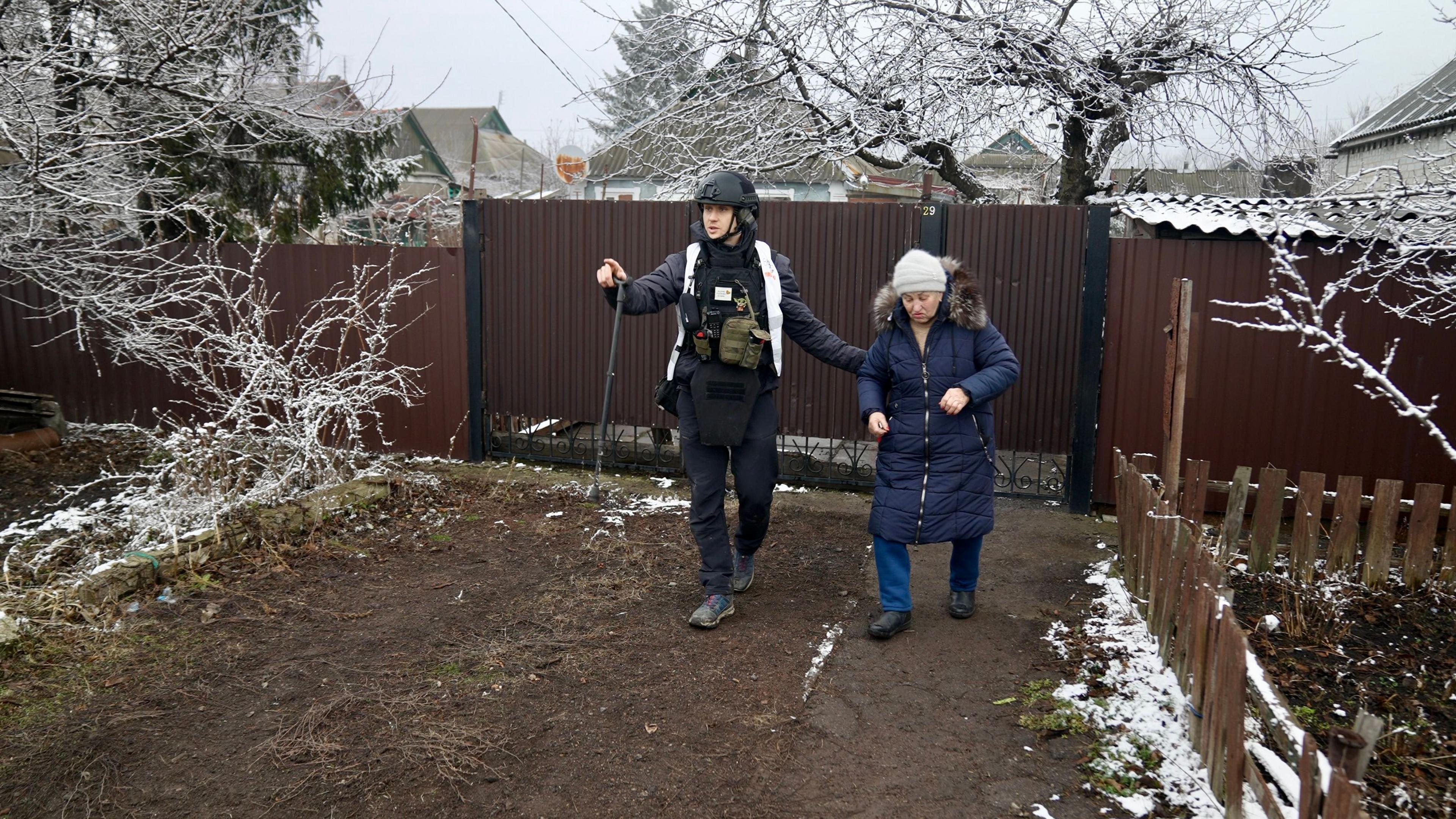 Anton Yaremchuk guides an elderly woman outside her home
